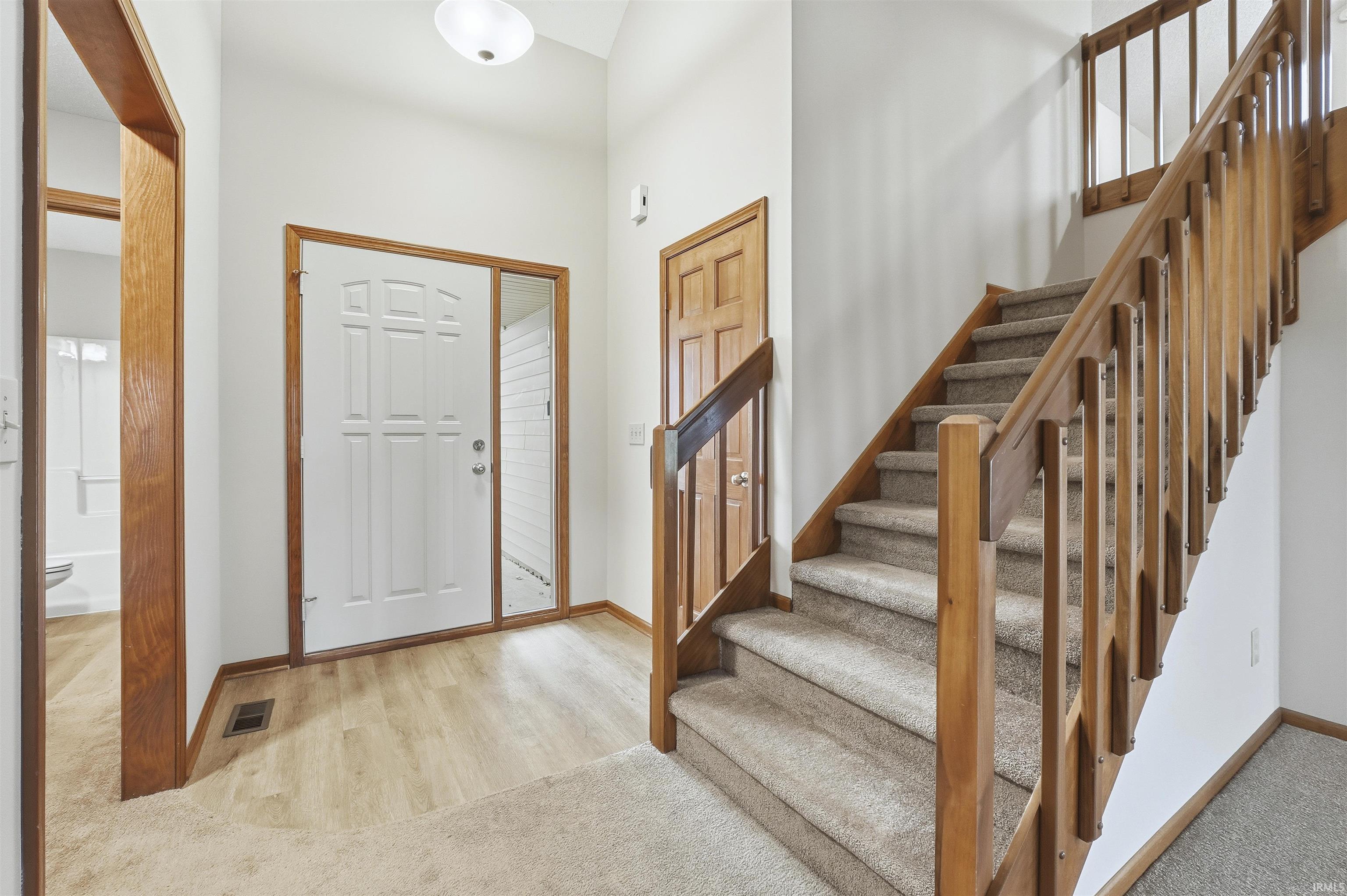 Foyer with stairway, light colored carpet, light wood finished floors, and a towering ceiling