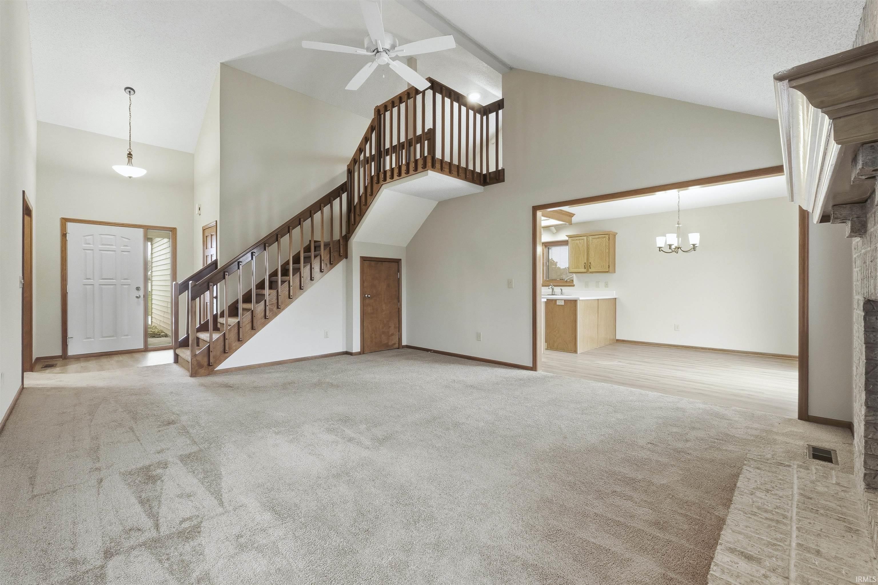 Unfurnished living room featuring high vaulted ceiling, light carpet, a chandelier, stairway, and a ceiling fan