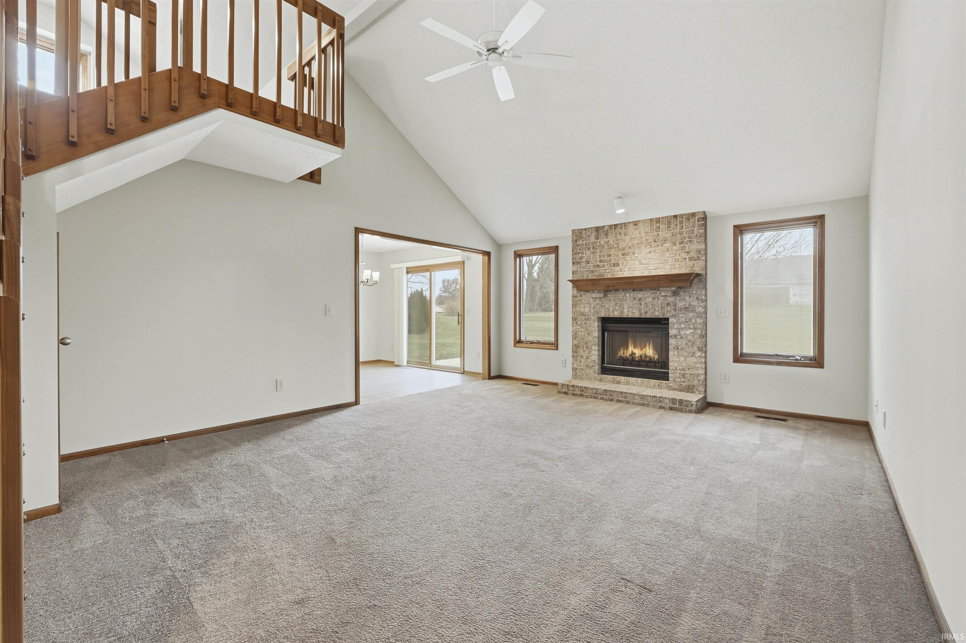 Unfurnished living room featuring high vaulted ceiling, light carpet, a fireplace, and ceiling fan