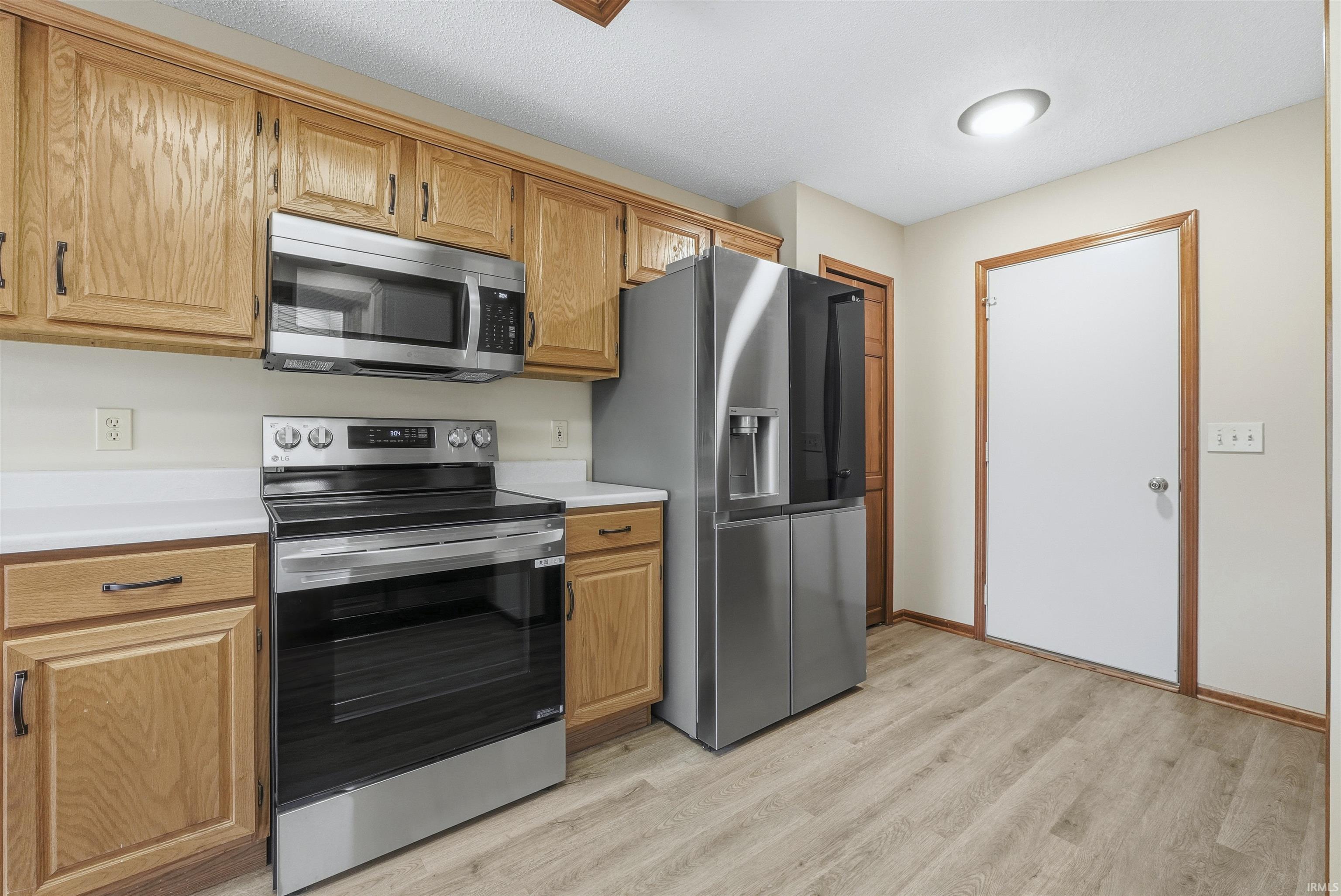 Kitchen featuring appliances with stainless steel finishes, light countertops, light wood-style flooring, and brown cabinetry