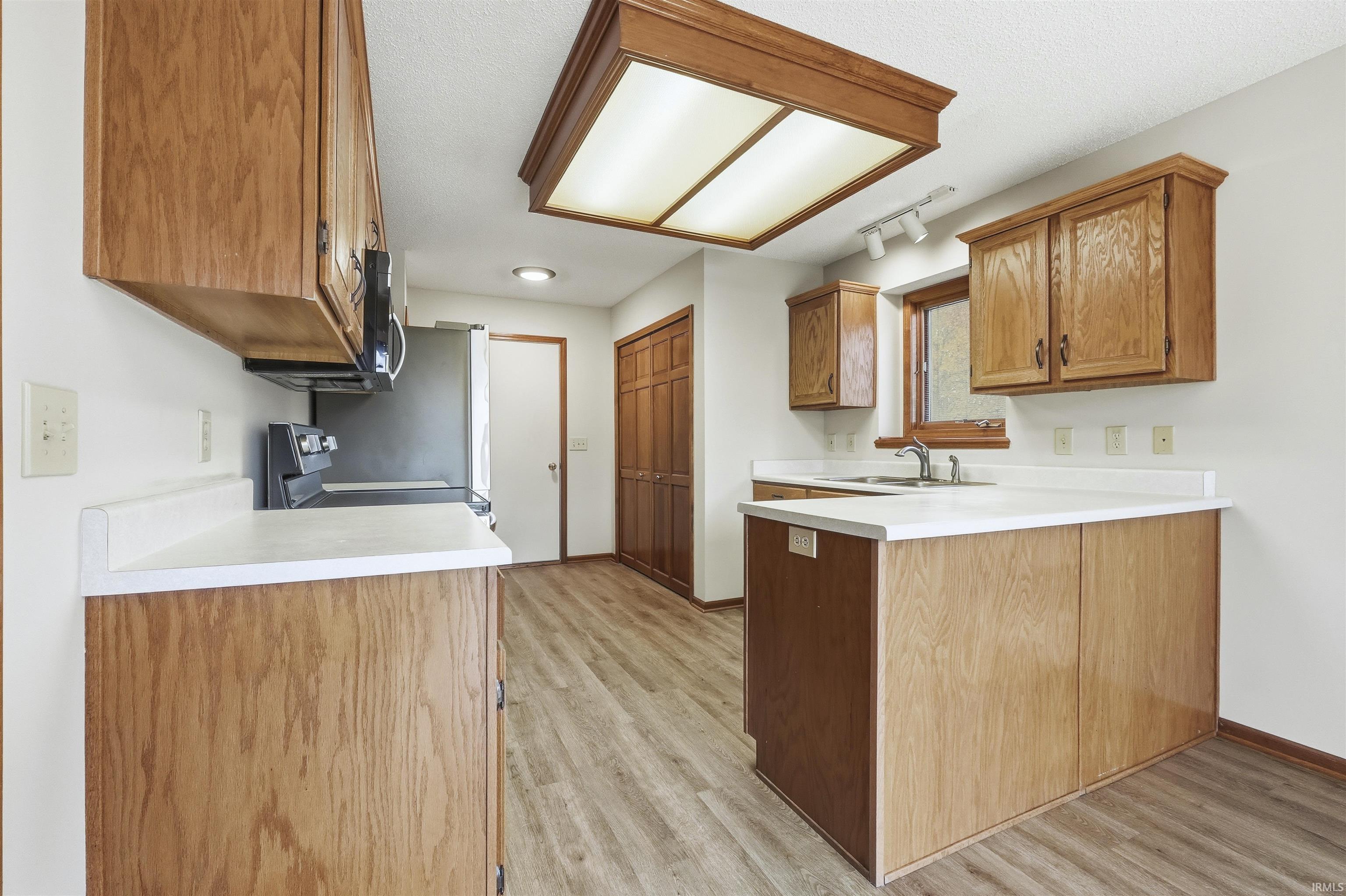 Kitchen with a peninsula, light countertops, brown cabinetry, light wood-style floors, and a textured ceiling