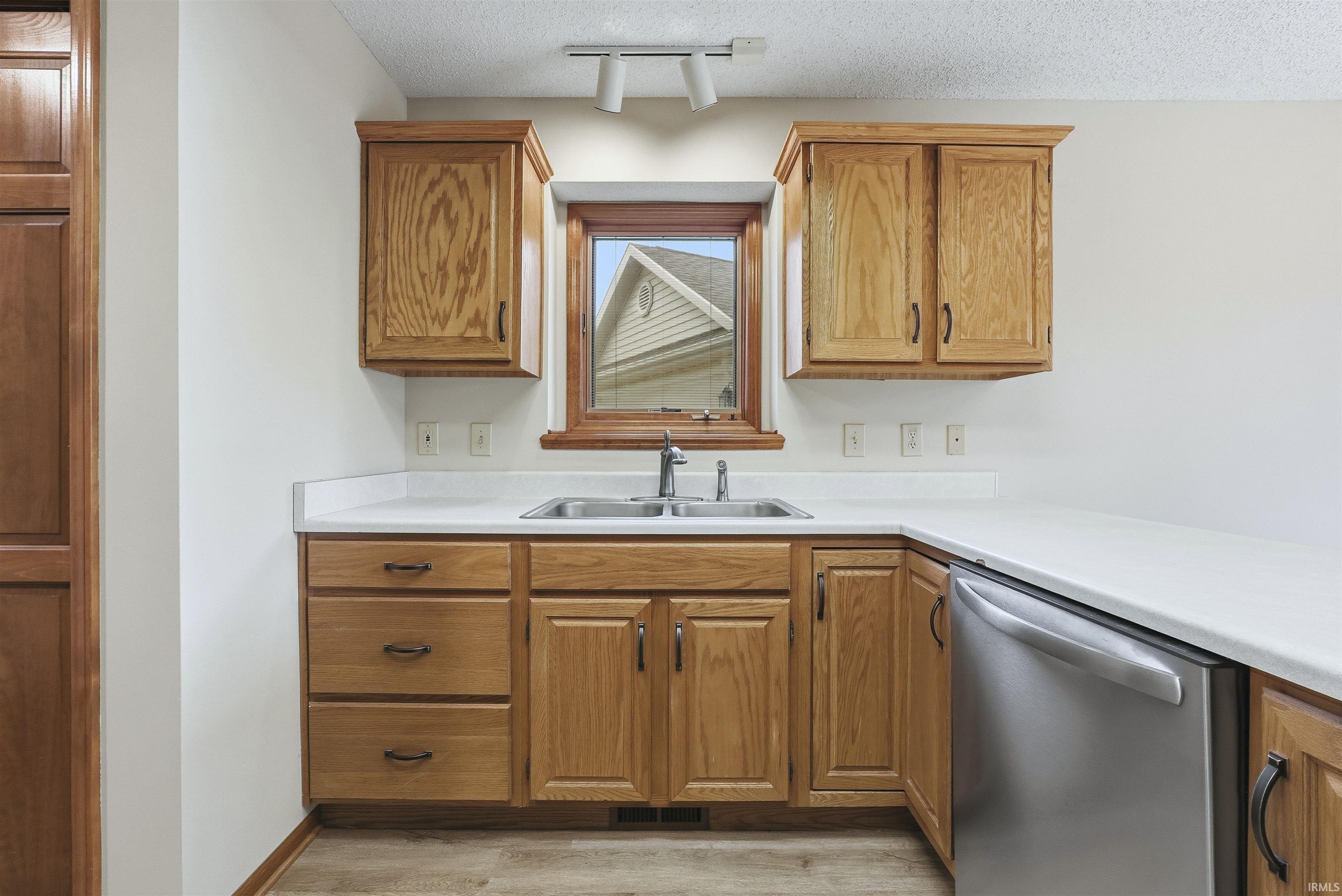 Kitchen featuring a textured ceiling, light countertops, dishwasher, brown cabinetry, and light wood-style flooring