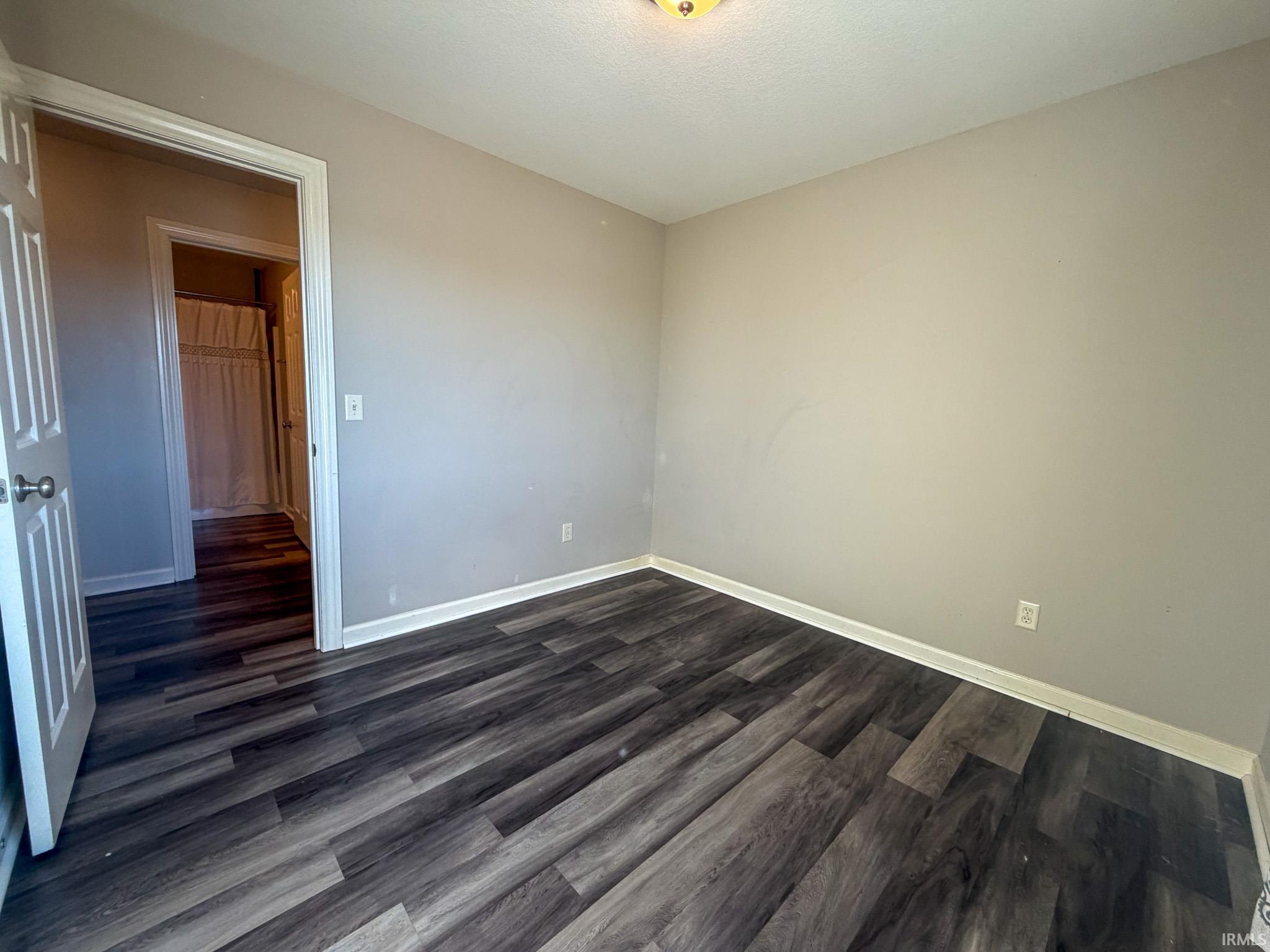 Unfurnished room featuring dark wood-style floors and baseboards