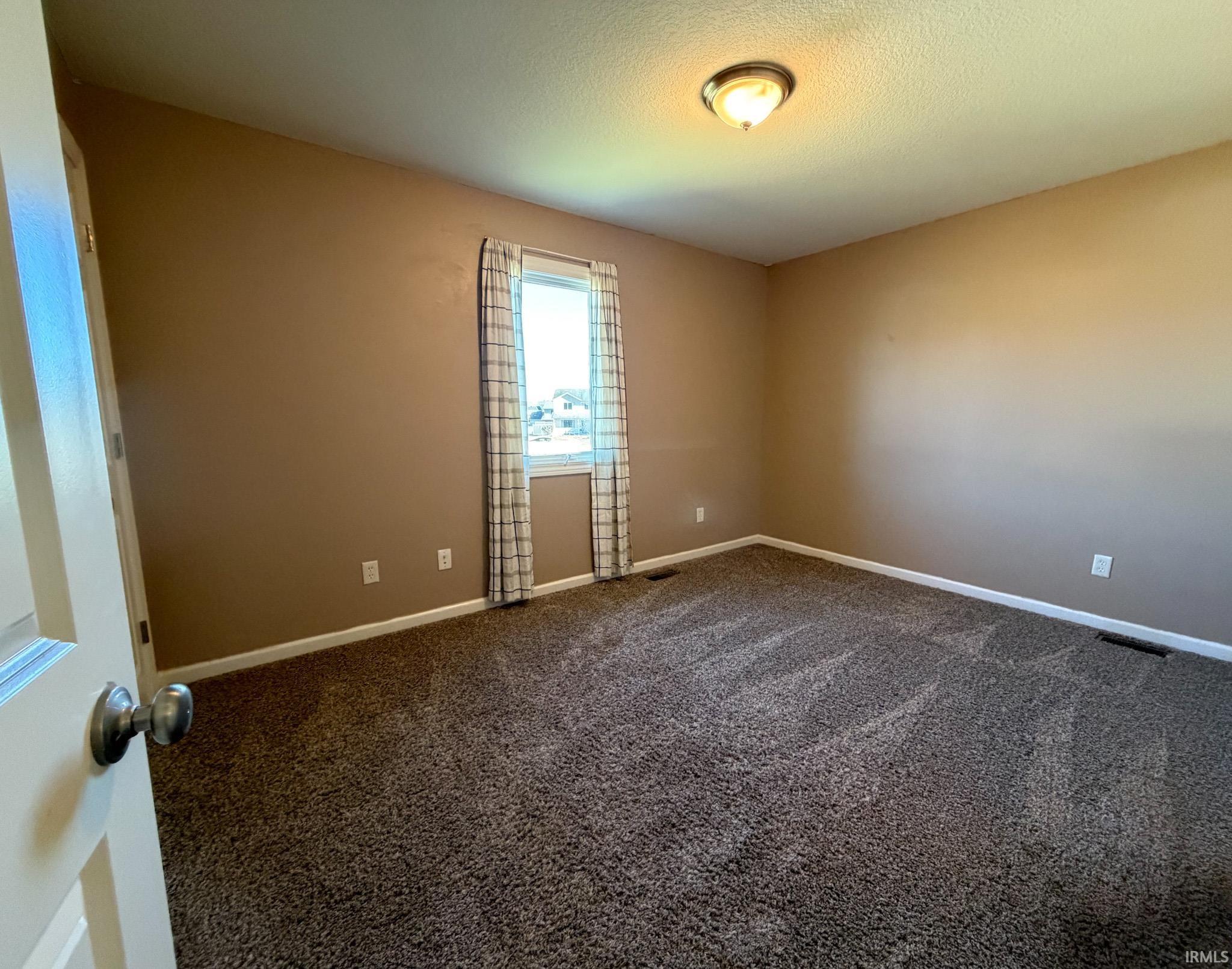 Carpeted spare room featuring baseboards and a textured ceiling