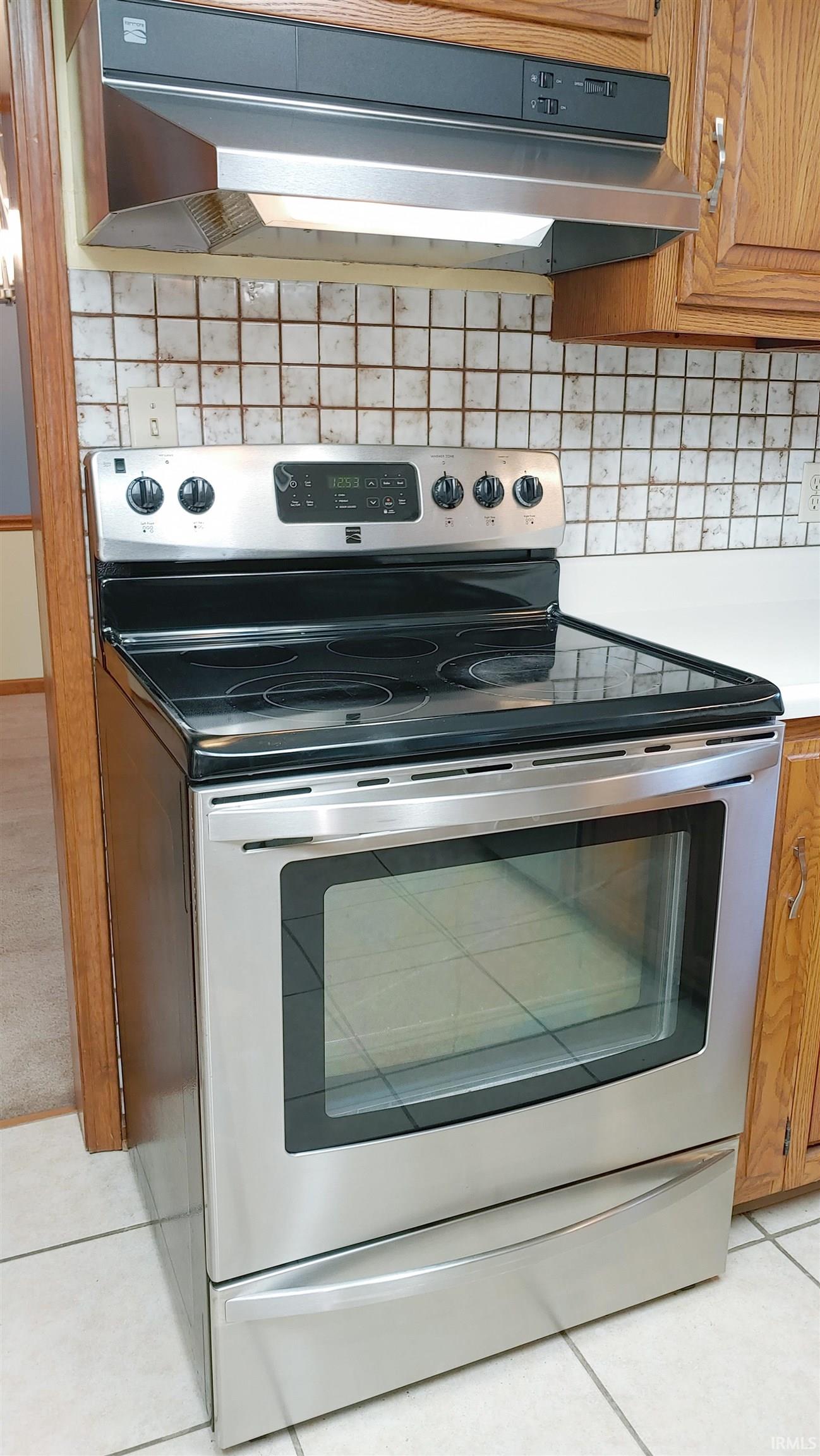Kitchen with stainless steel electric range with natural wood cabinets and under cabinet range hood