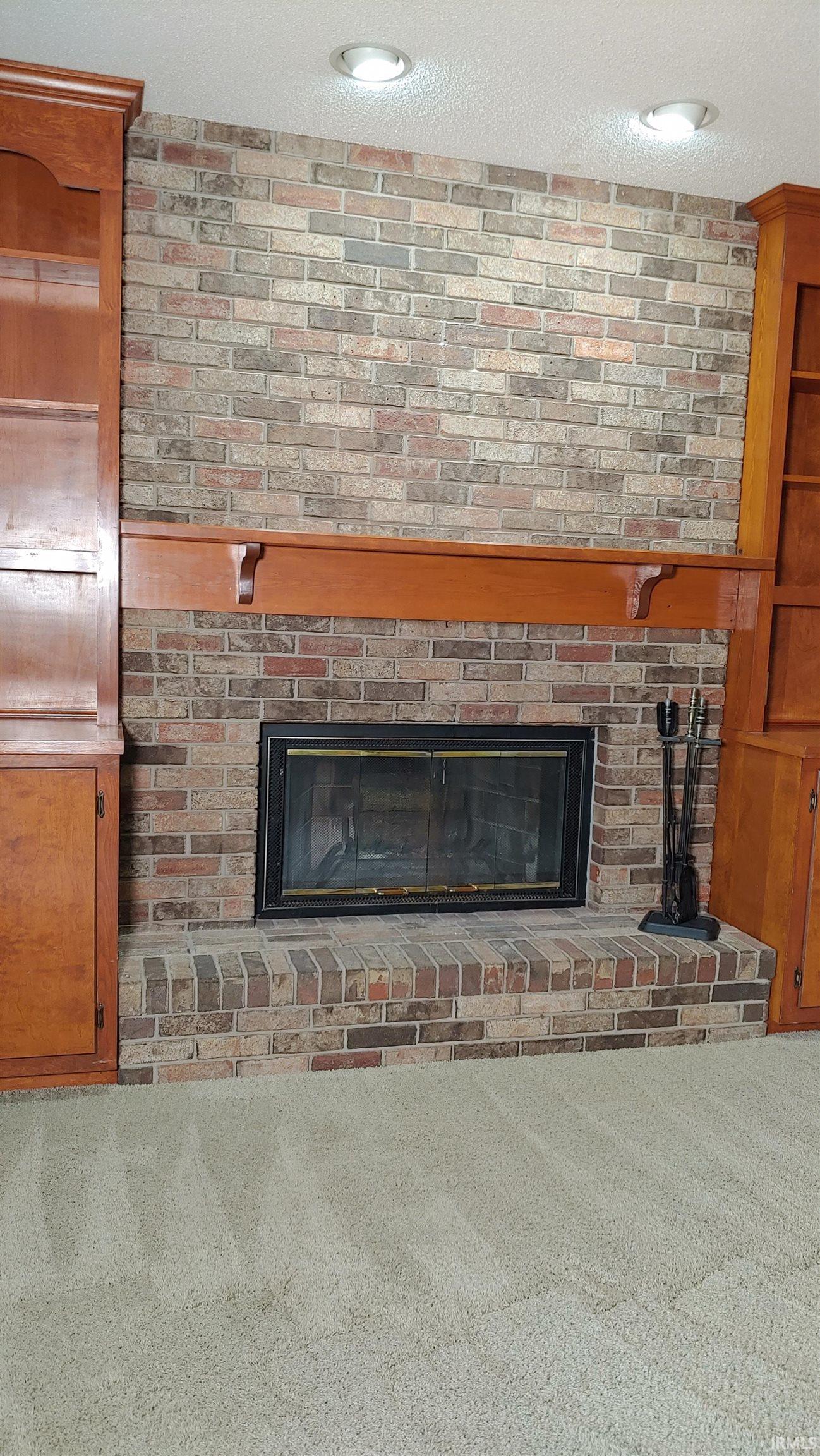Brick fireplace with mantel, carpet floors, and recessed lighting