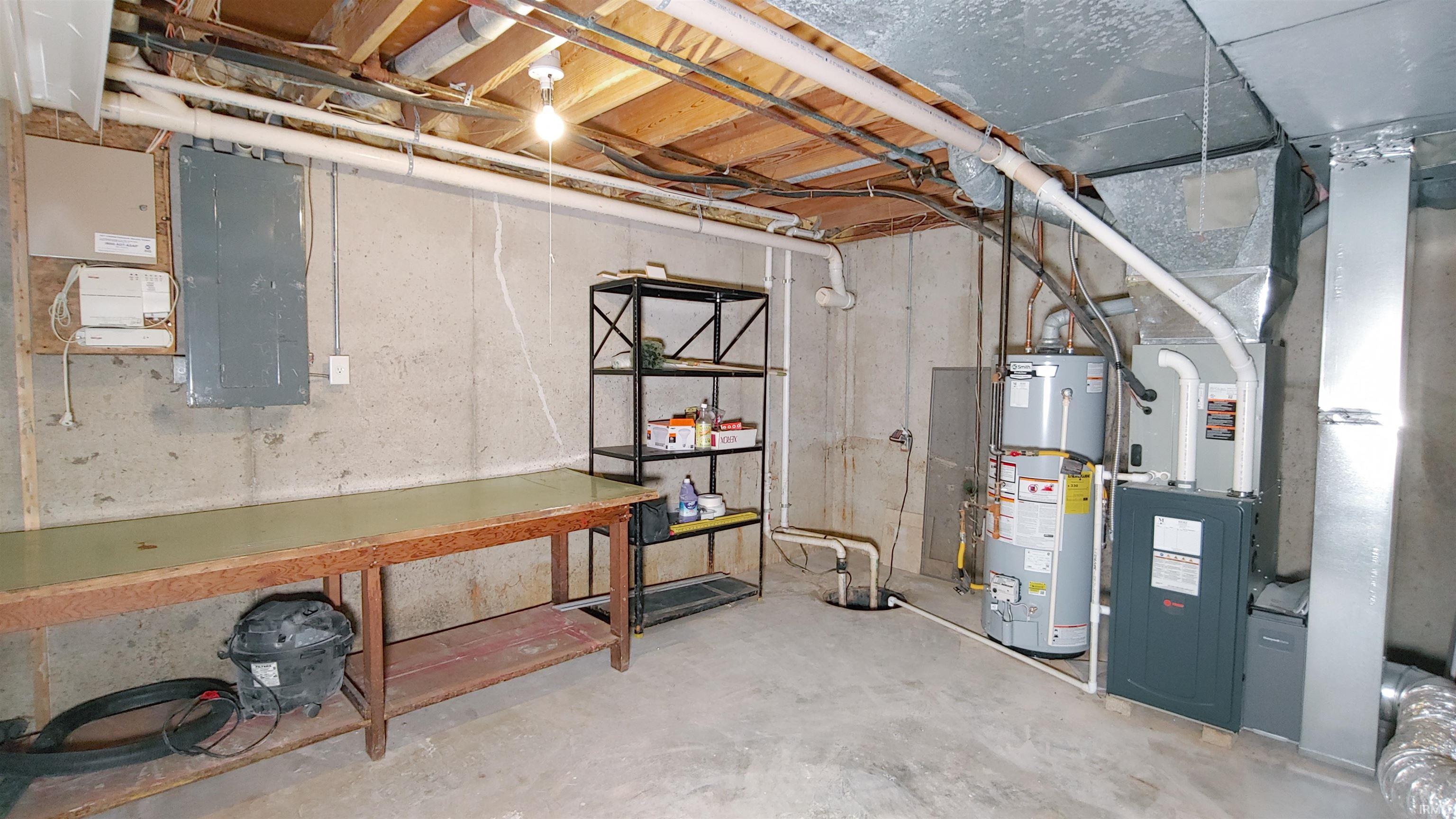 Unfinished utility room with workbench, electric panel, gas water heater, and furnace