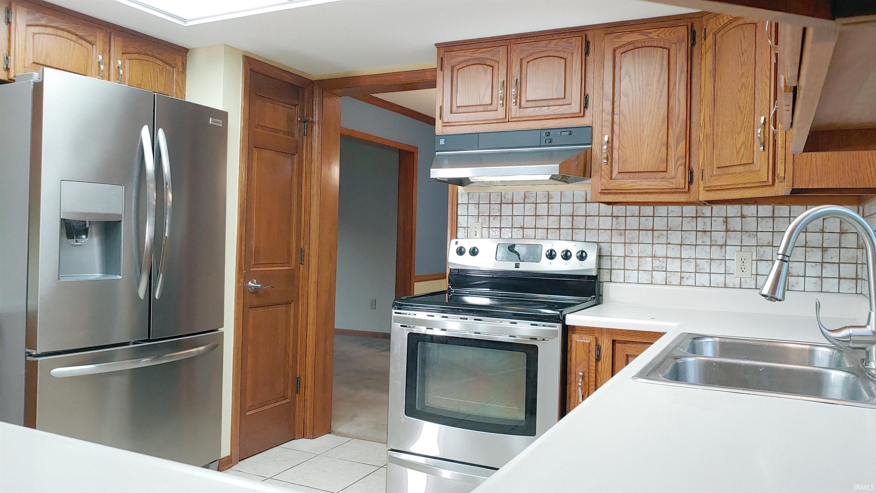 Kitchen featuring stainless steel appliances, natural wood cabinets, under cabinet range hood