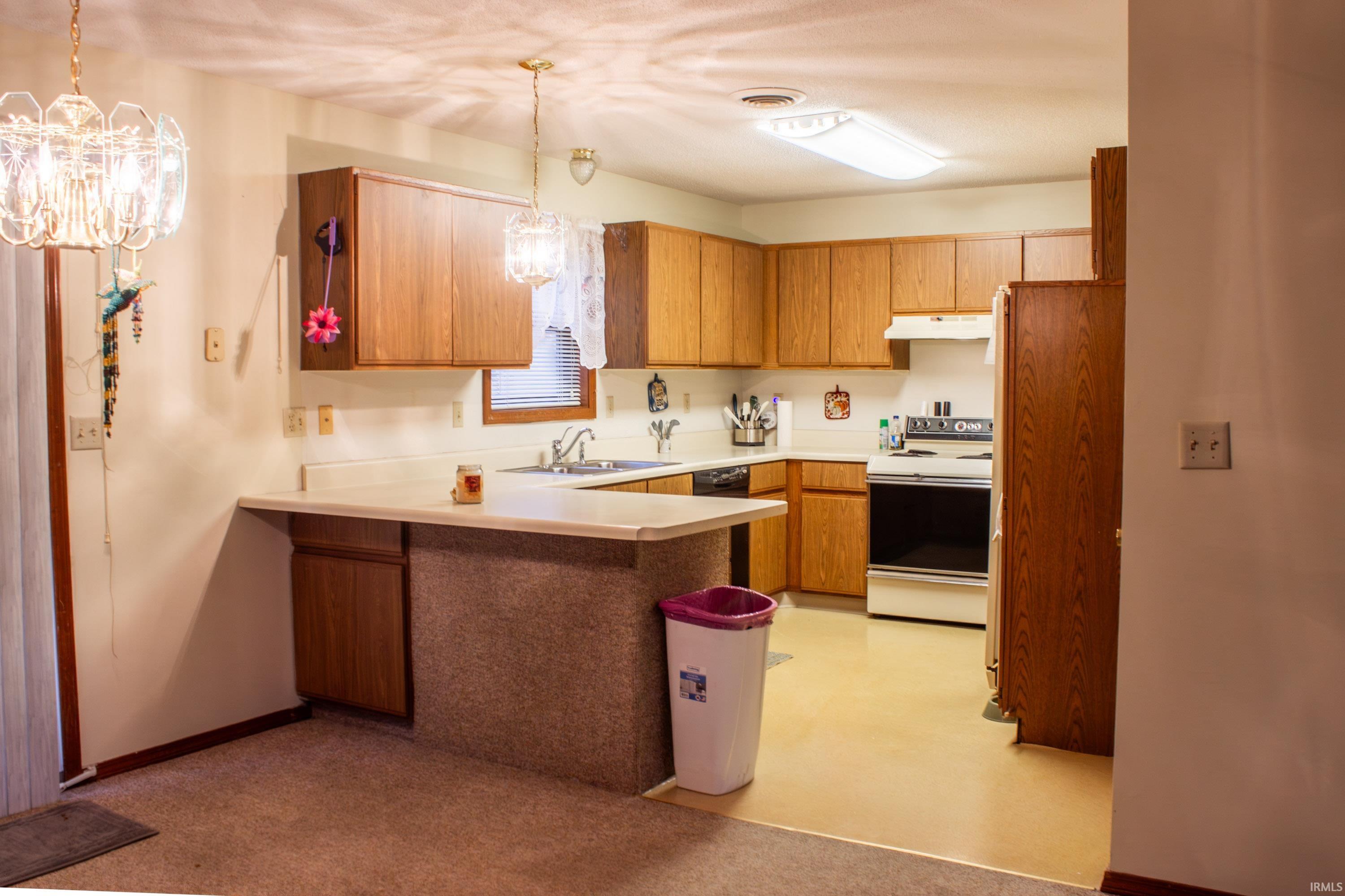 Kitchen with light countertops, a peninsula, white electric range oven, hanging light fixtures, and brown cabinets