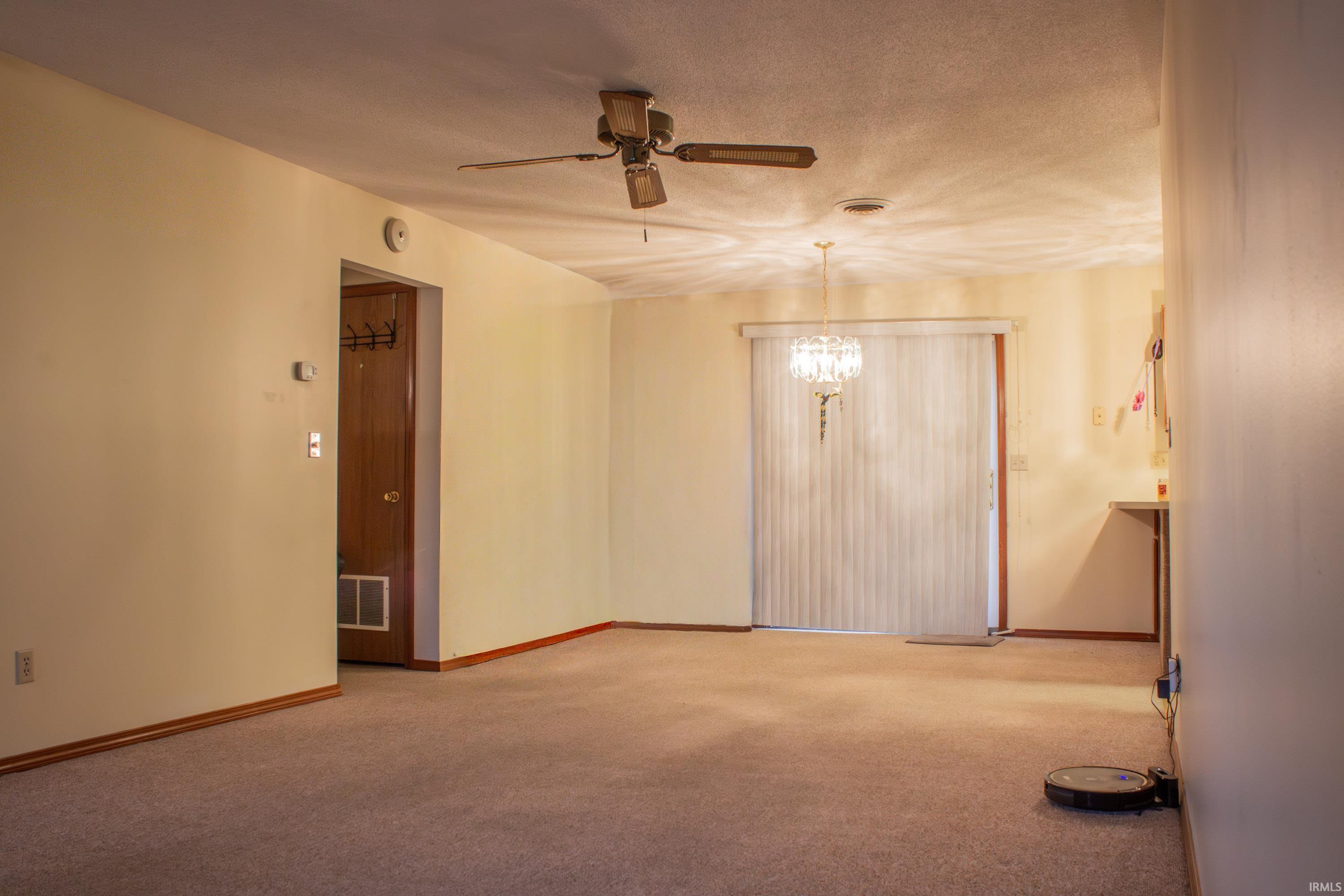 Empty room featuring light colored carpet, a textured ceiling, ceiling fan, and a chandelier
