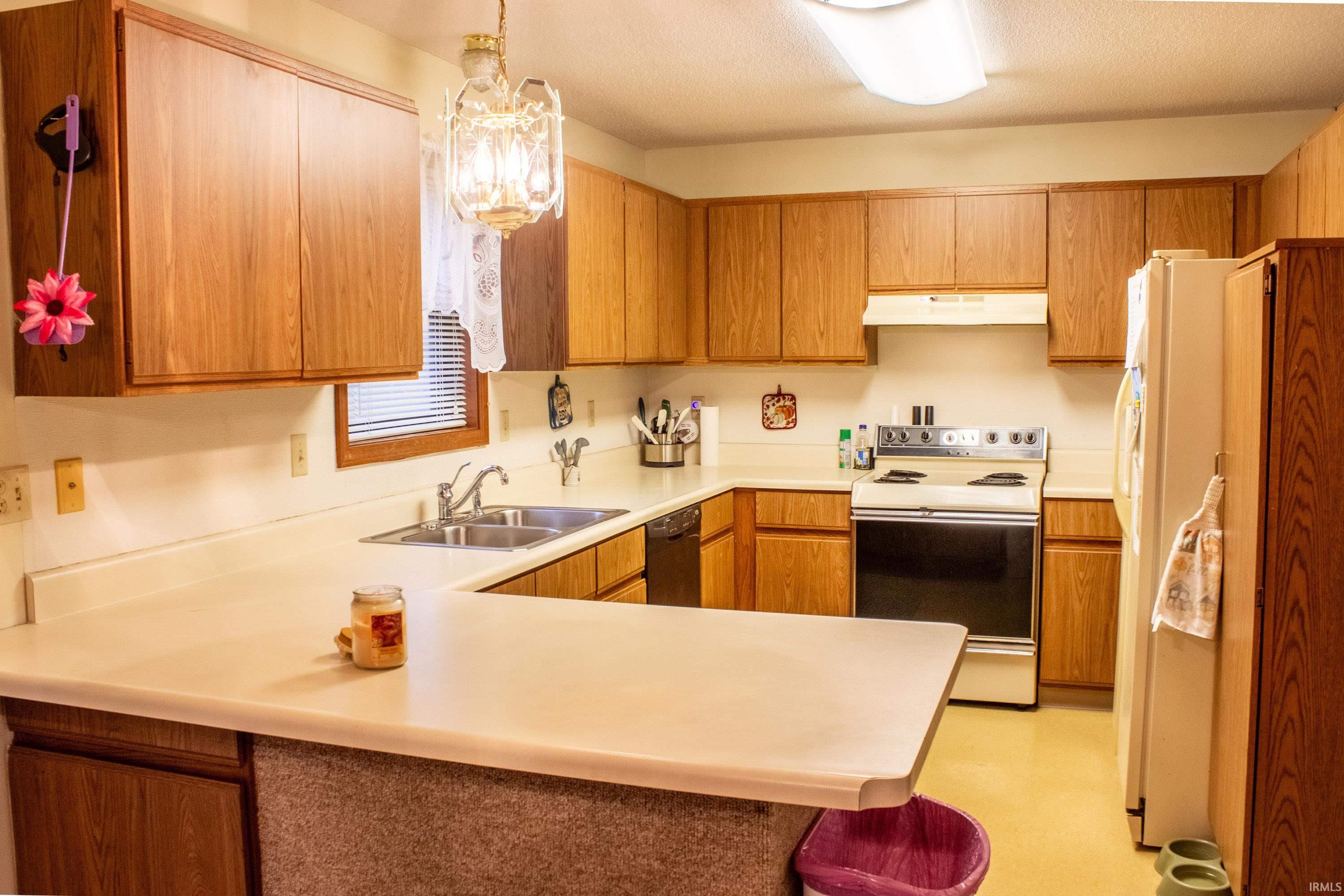 Kitchen featuring white appliances, light countertops, a peninsula, under cabinet range hood, and brown cabinets
