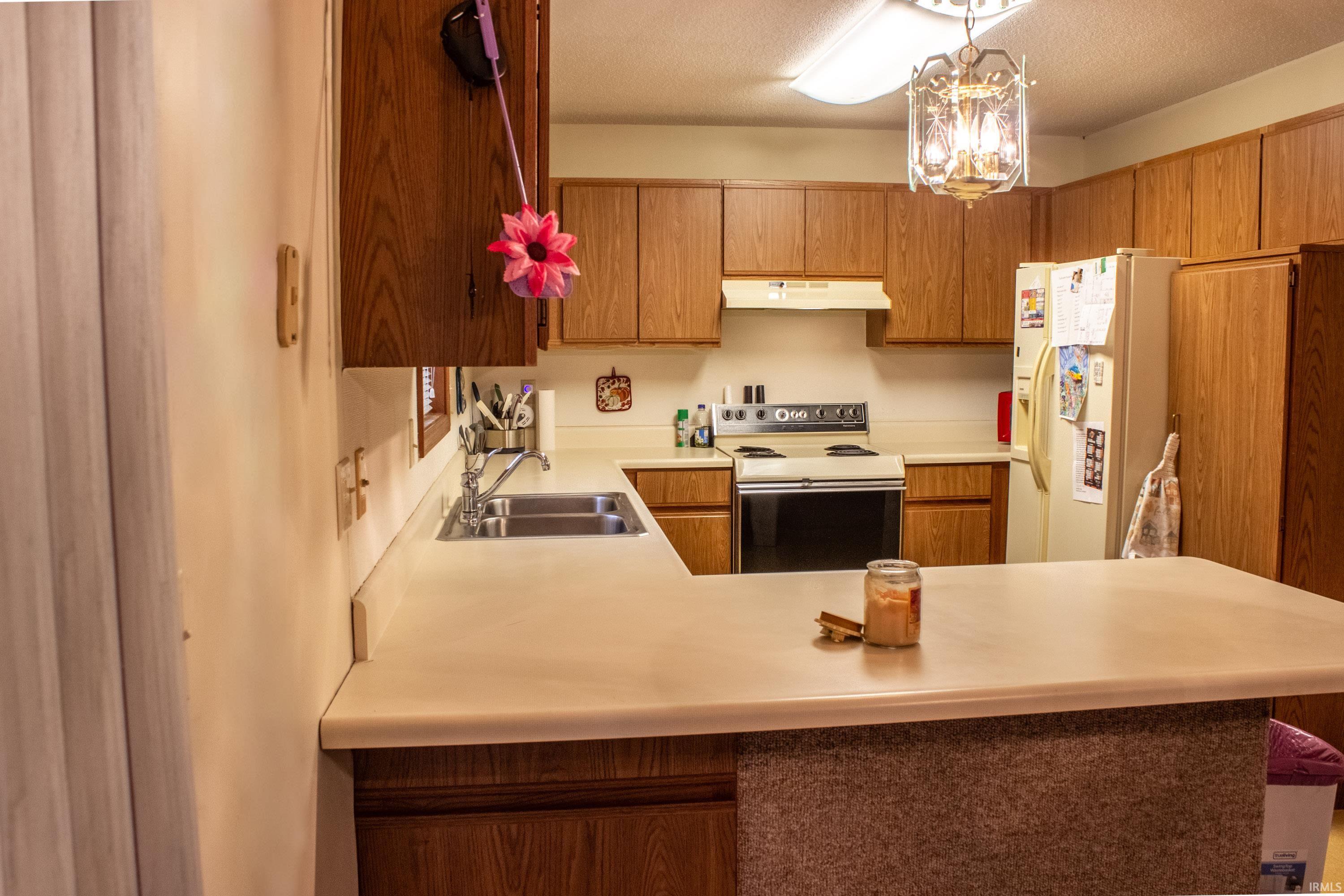 Kitchen featuring range with electric cooktop, light countertops, white refrigerator with ice dispenser, brown cabinets, and under cabinet range hood
