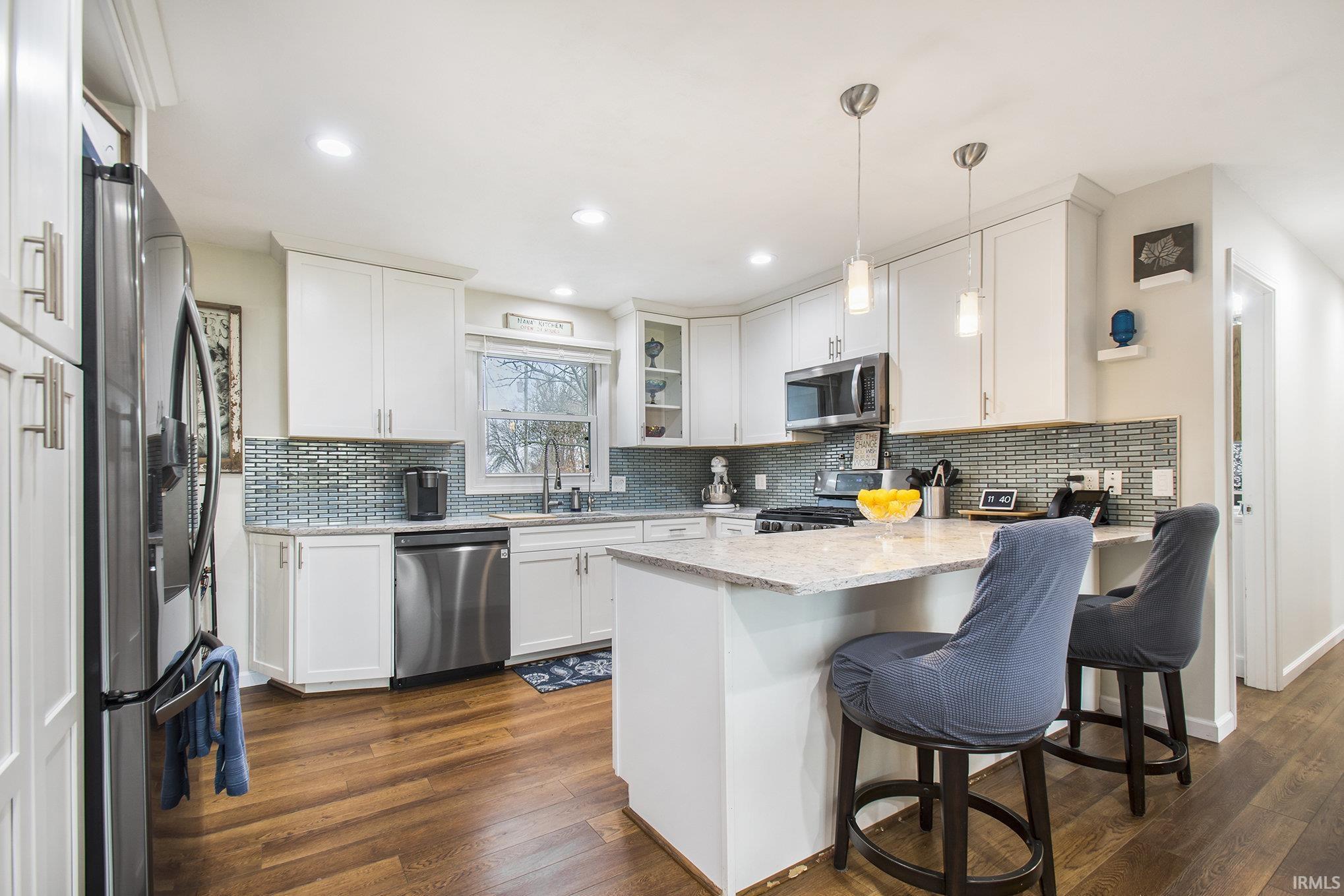 Kitchen with a peninsula, white custom cabinetry, decorative backsplash, appliances with stainless steel finishes, and recessed lighting