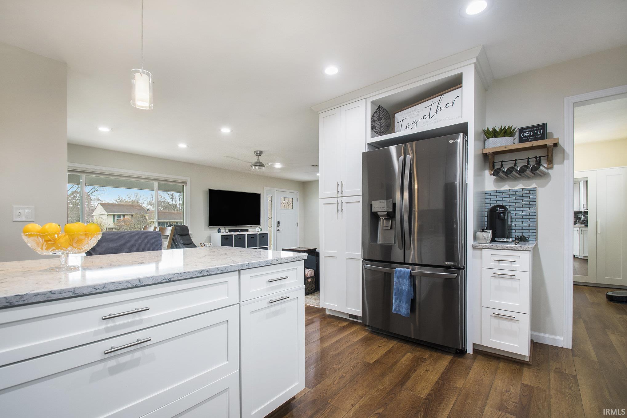 Kitchen with stainless steel fridge, white cabinetry, light stone countertops, open shelves, and recessed lighting