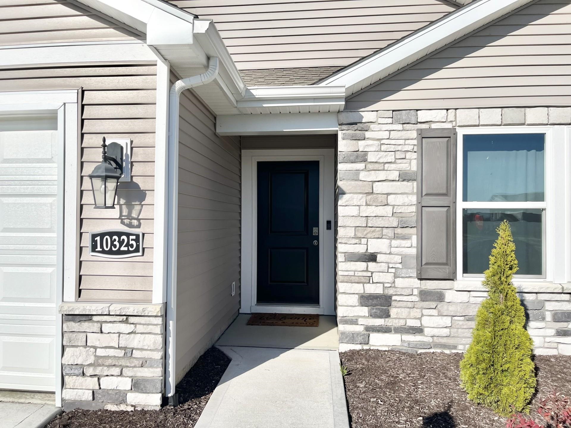 Doorway to property featuring stone siding, a garage, and roof with shingles