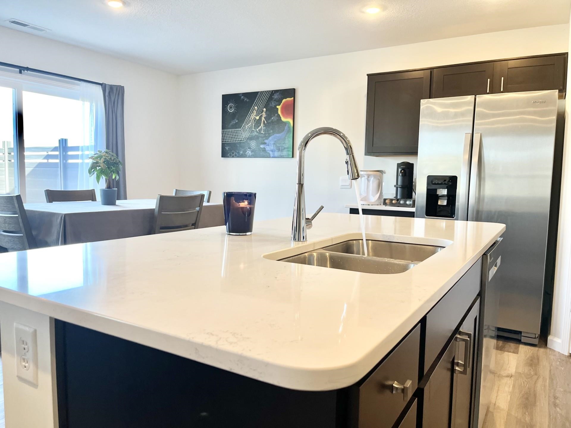Kitchen featuring dark cabinetry, an island with sink, stainless steel appliances, light wood-style flooring, and light stone countertops