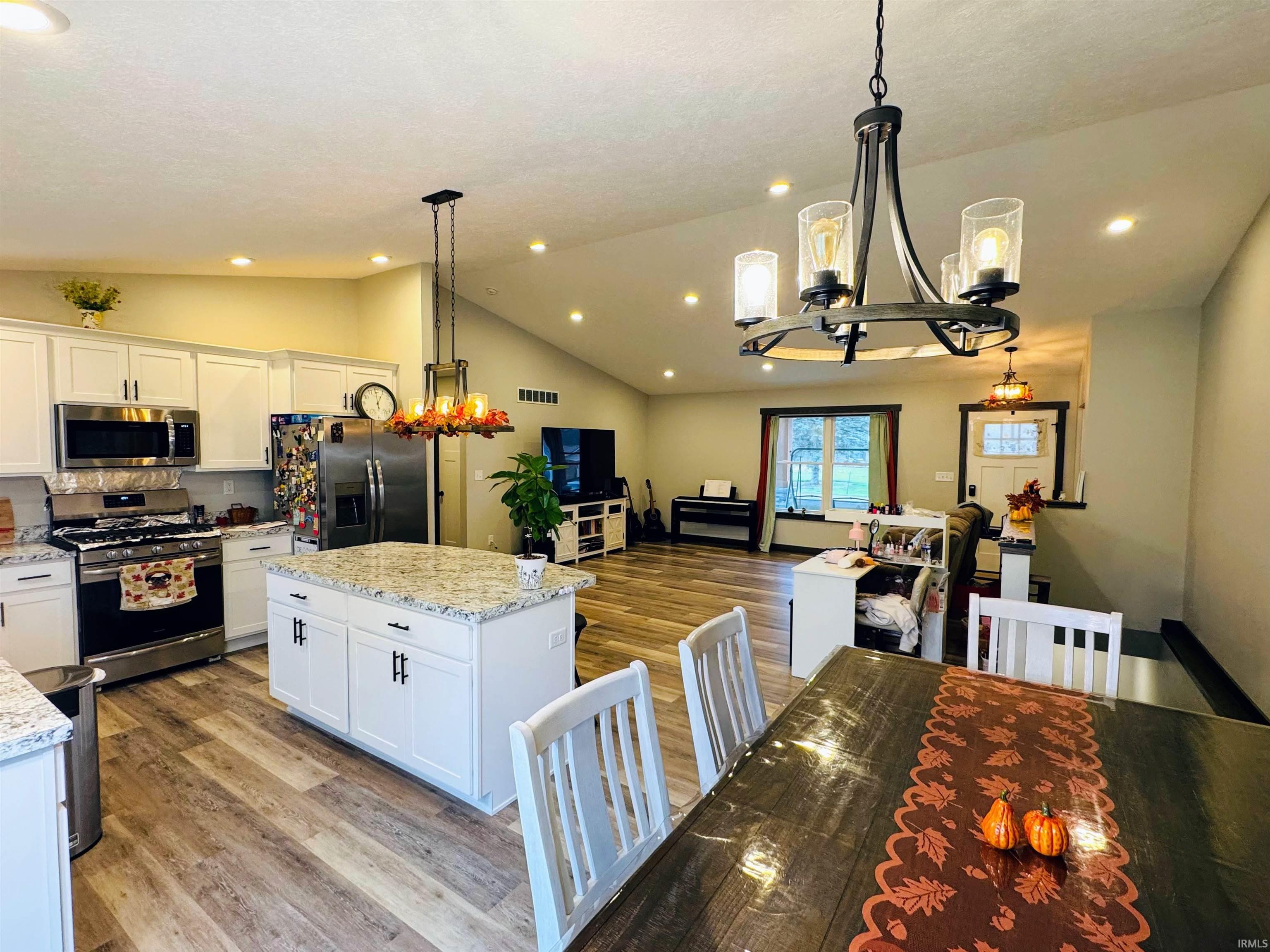 Kitchen with a chandelier, white cabinetry, appliances with stainless steel finishes, pendant lighting, and lofted ceiling