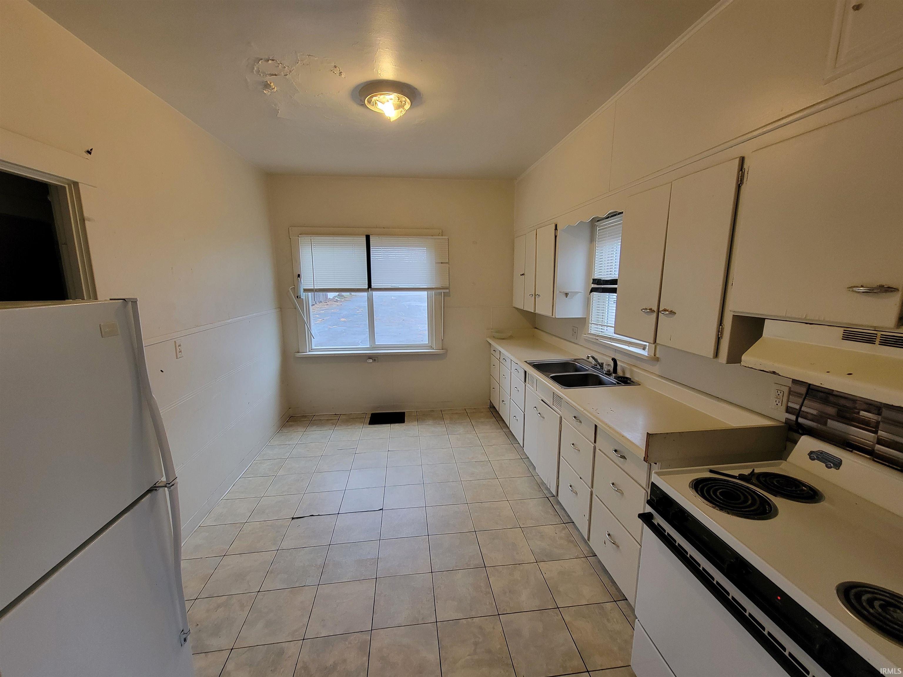 Kitchen featuring white appliances, light countertops, range hood, white cabinets, and light tile patterned flooring