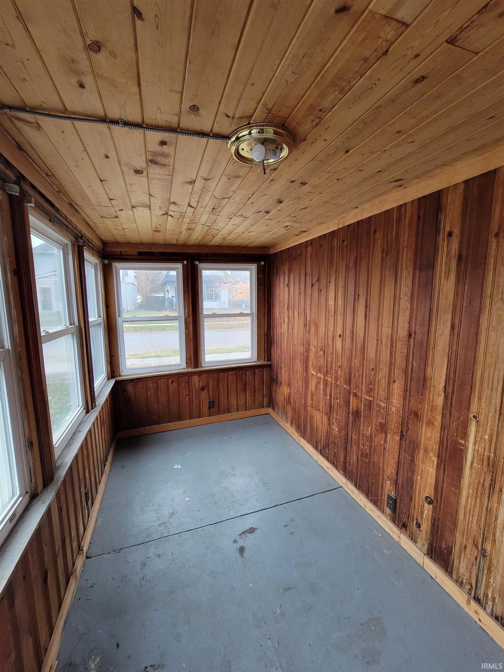 Unfurnished sunroom with wood walls, unfinished concrete flooring, and wooden ceiling
