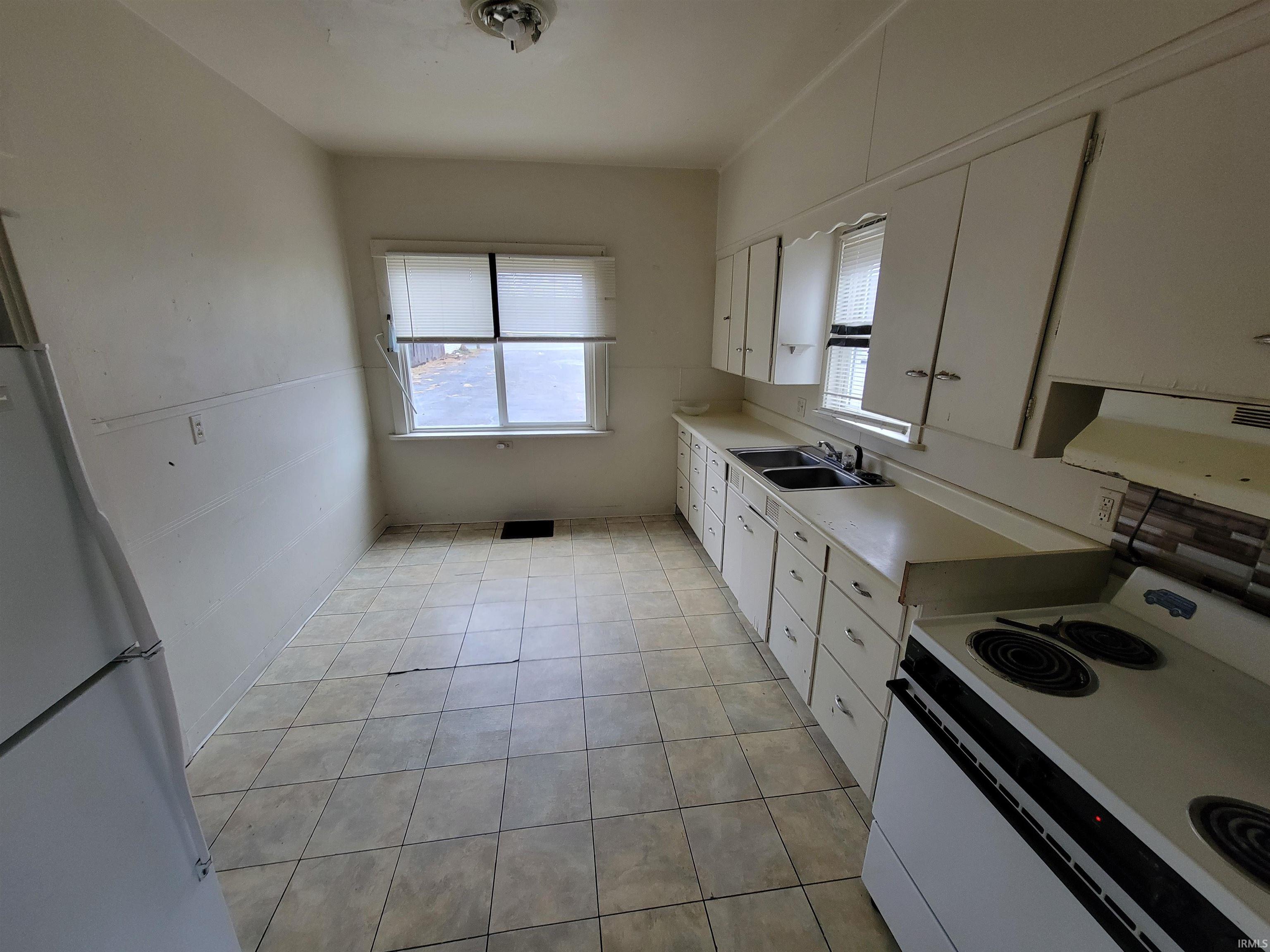 Kitchen with light countertops, white cabinetry, white appliances, light tile patterned floors, and range hood