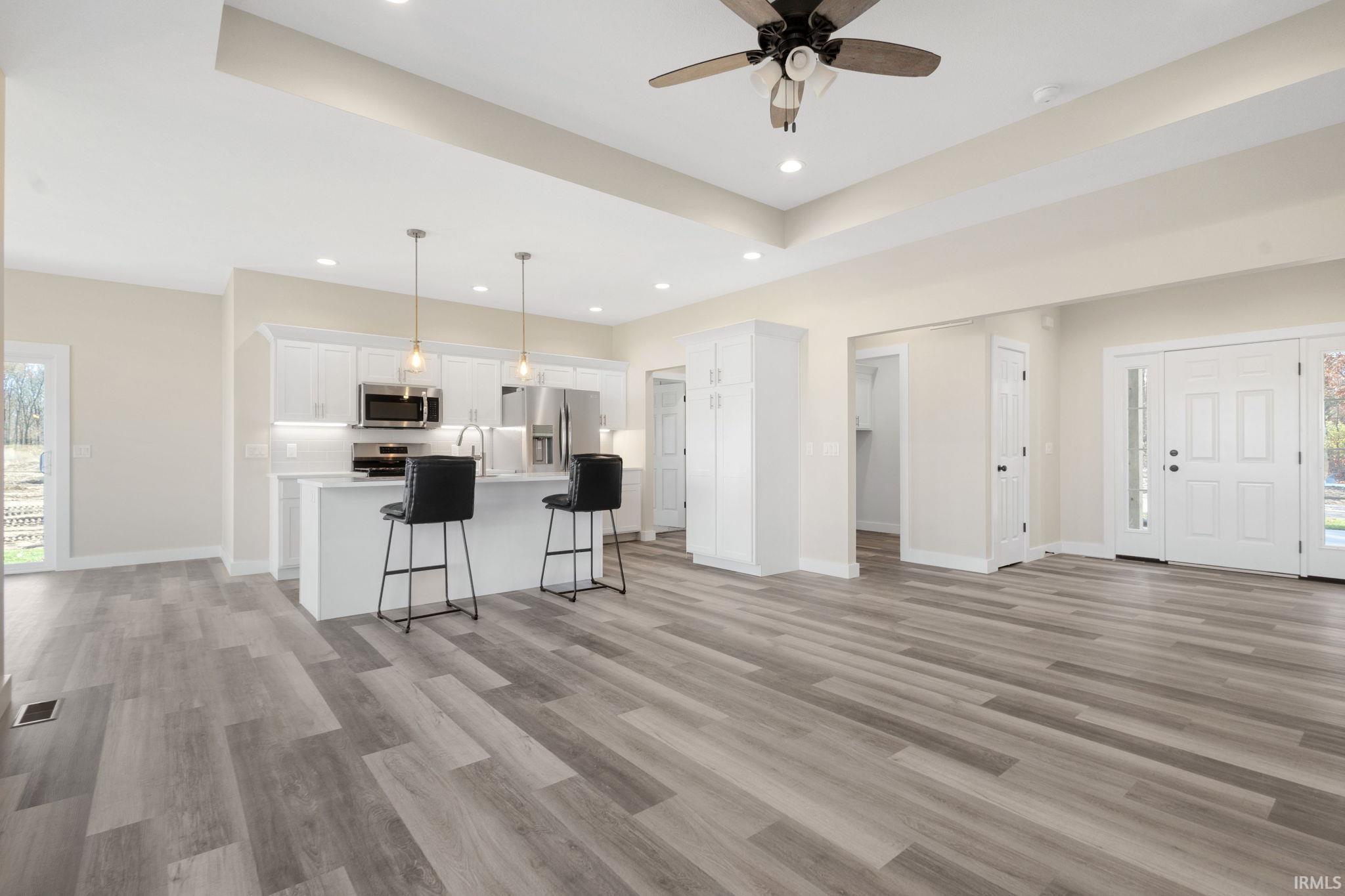 Kitchen featuring white cabinetry, a kitchen bar, open floor plan, an island with sink, and decorative light fixtures