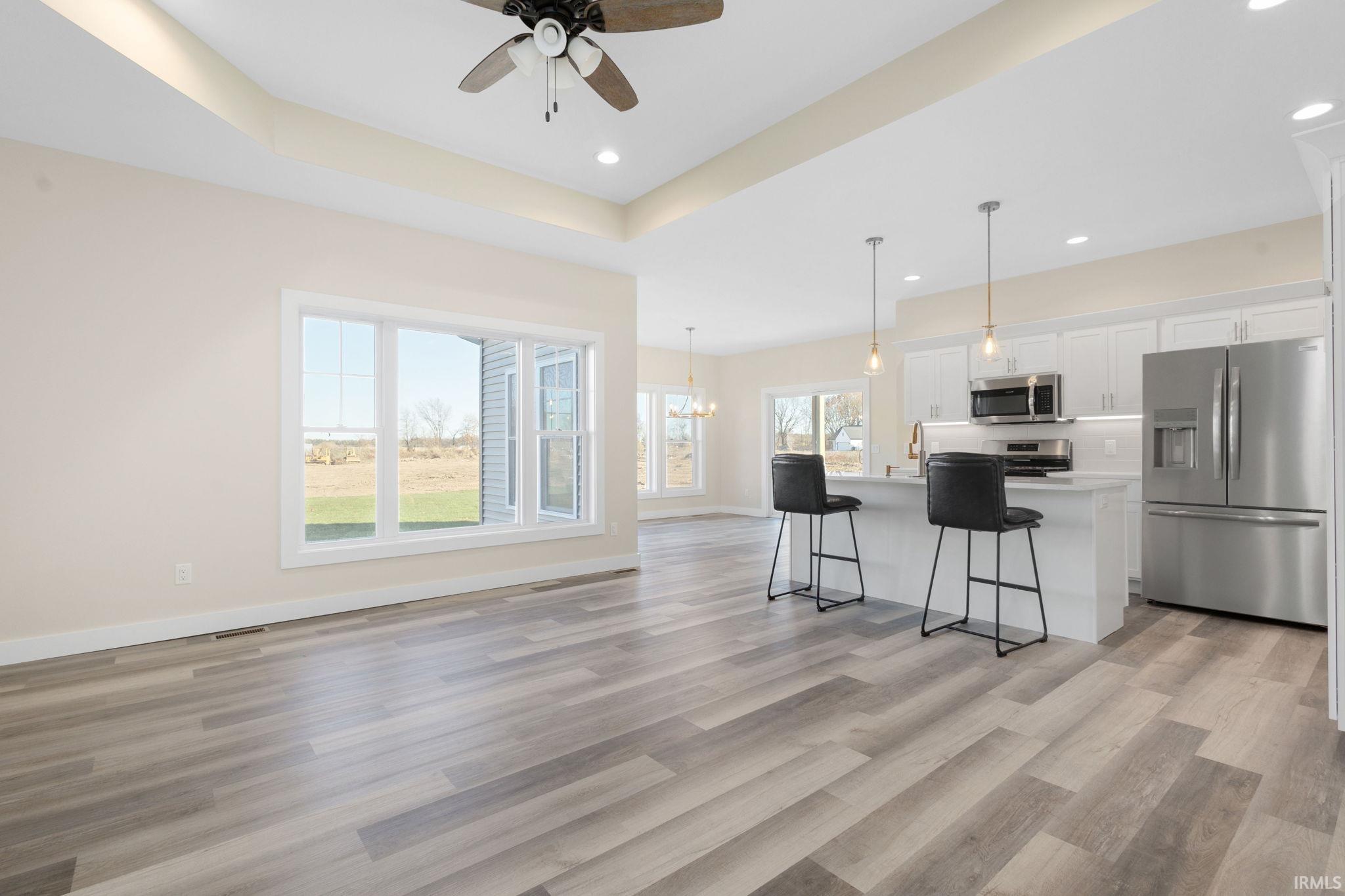 Kitchen with stainless steel appliances, white cabinets, open floor plan, hanging light fixtures, and a raised ceiling