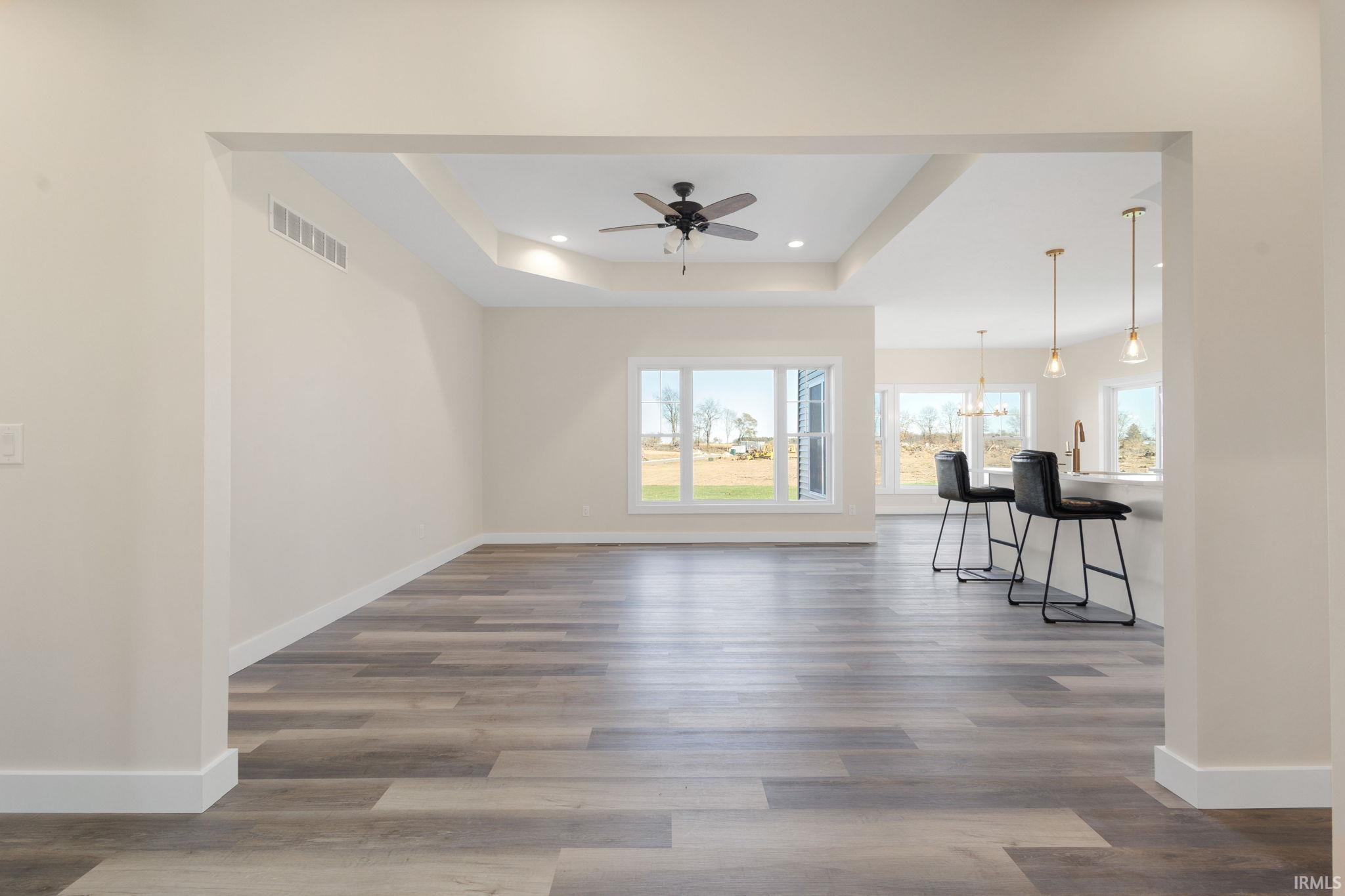 Unfurnished living room with a tray ceiling, recessed lighting, dark wood-style floors, ceiling fan, and a chandelier