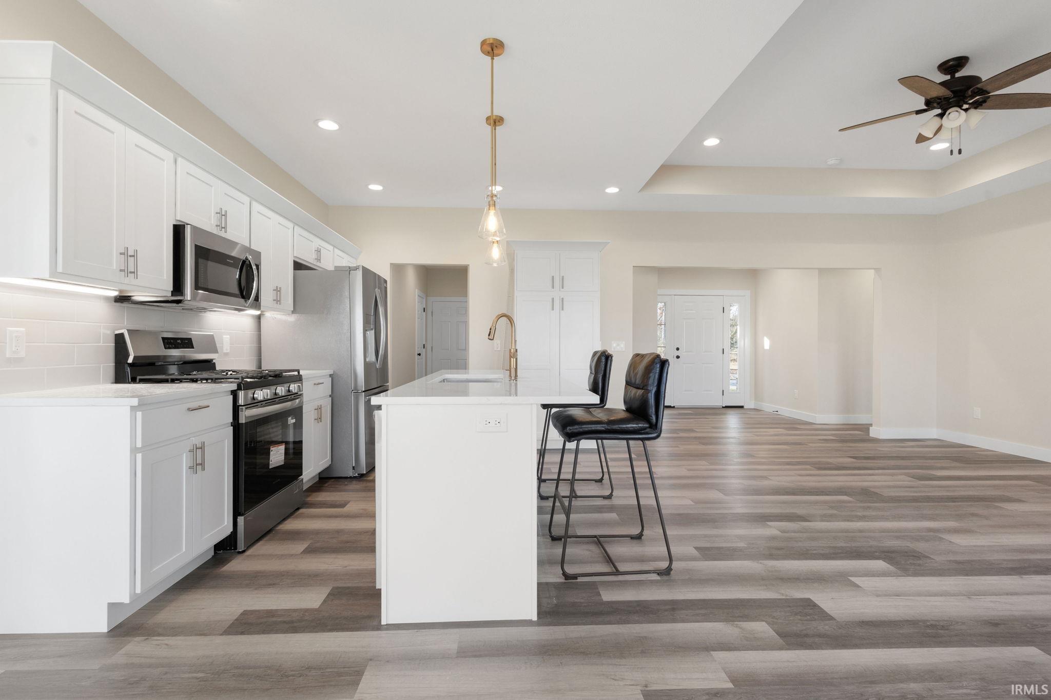 Kitchen with stainless steel appliances, a breakfast bar area, white cabinetry, pendant lighting, and recessed lighting