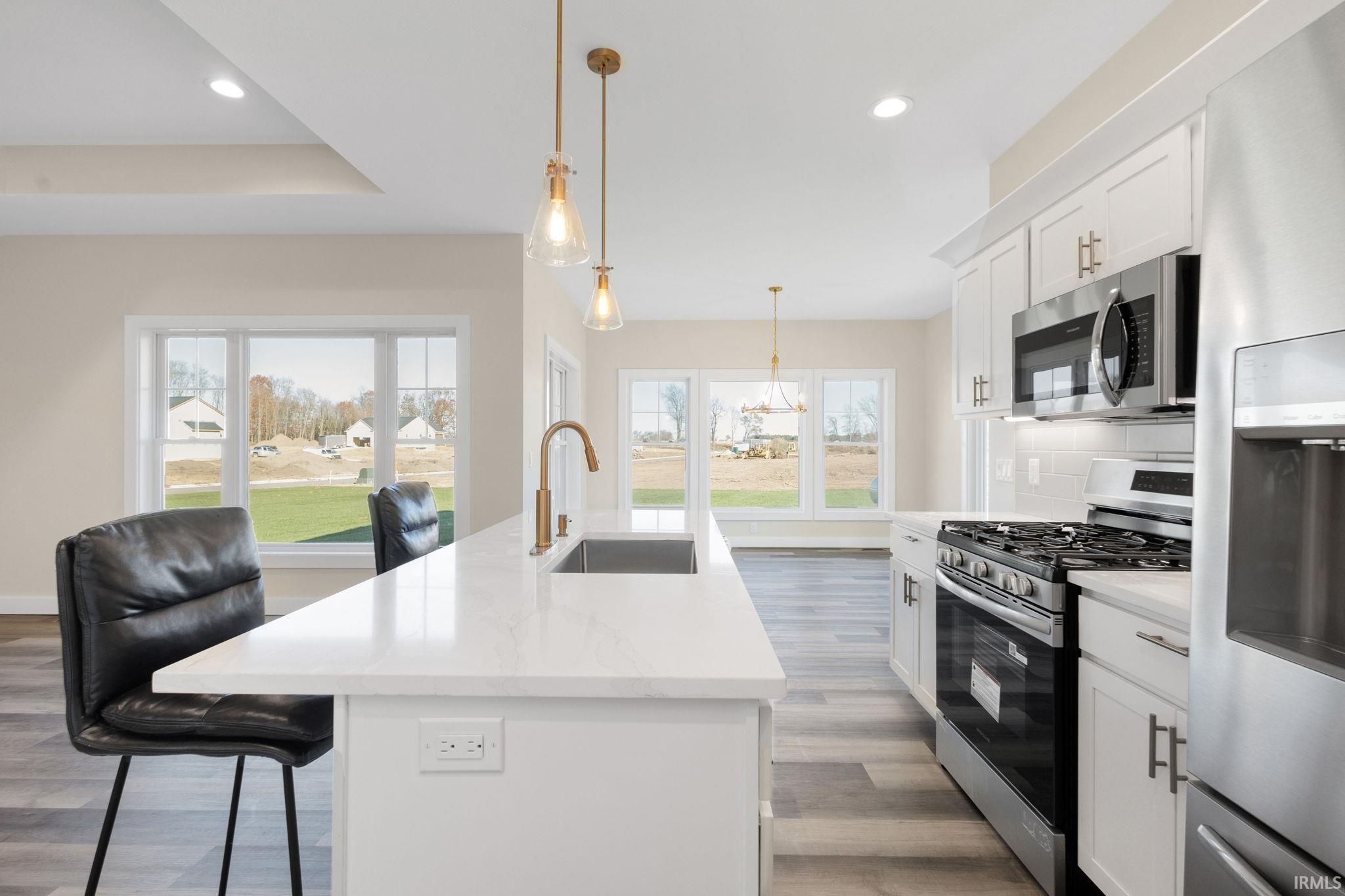 Kitchen with appliances with stainless steel finishes, white cabinetry, hanging light fixtures, recessed lighting, and an island with sink