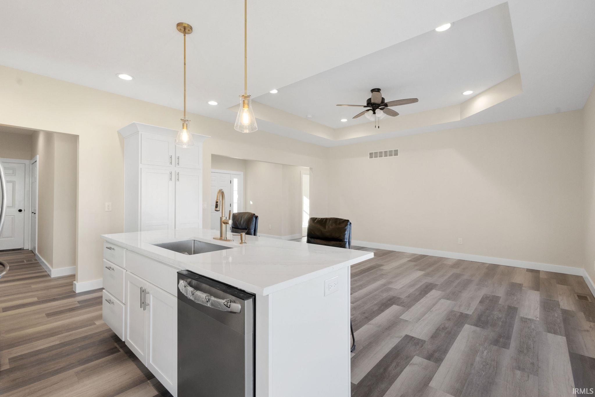 Kitchen featuring white cabinetry, open floor plan, hanging light fixtures, a kitchen island with sink, and stainless steel dishwasher