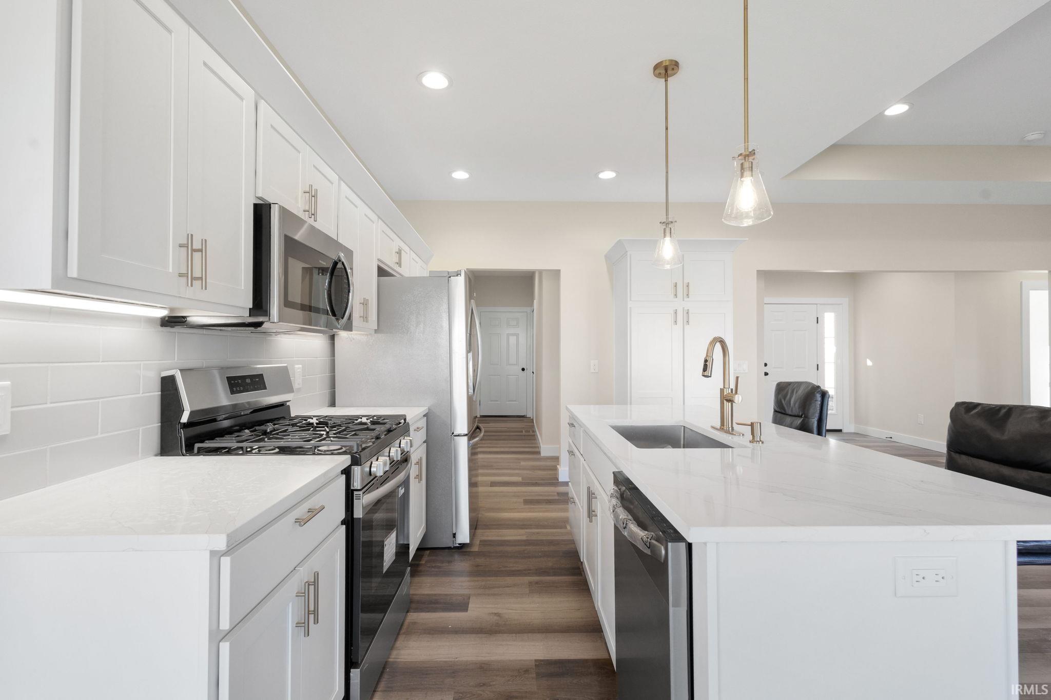 Kitchen with appliances with stainless steel finishes, dark wood finished floors, open floor plan, tasteful backsplash, and white cabinetry