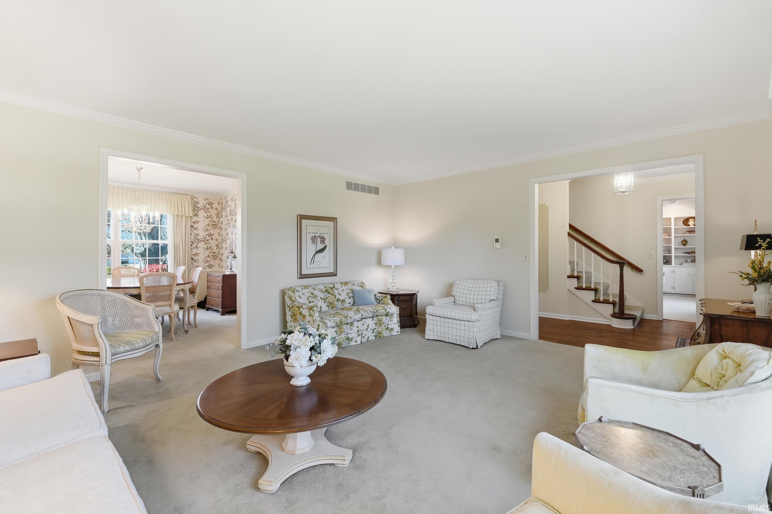 Living room with a chandelier, stairway, ornamental molding, and carpet floors