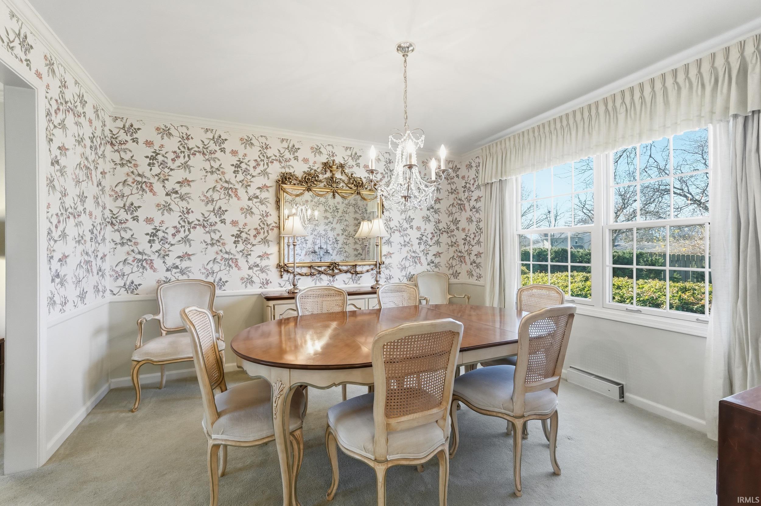 Carpeted dining area featuring wallpapered walls, a chandelier, a baseboard heating unit, crown molding, and a wainscoted wall