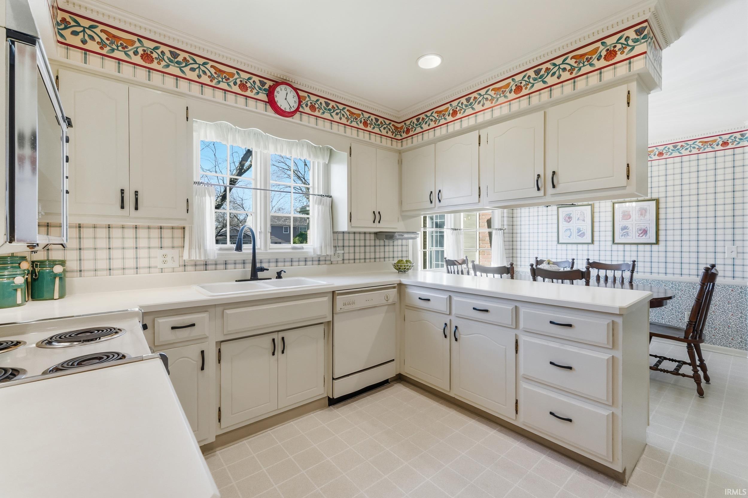 Kitchen with a peninsula, light countertops, white dishwasher, decorative backsplash, and ornamental molding
