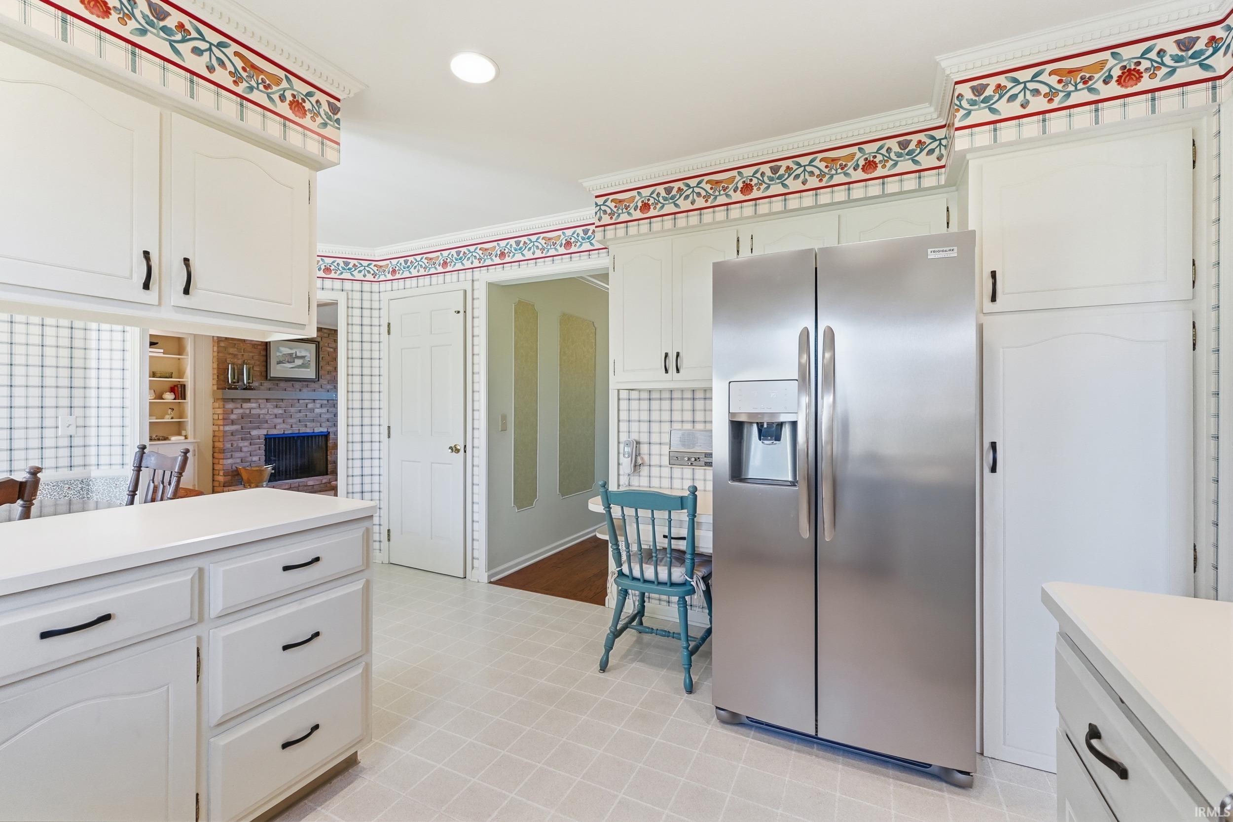 Kitchen featuring stainless steel refrigerator with ice dispenser, light countertops, white cabinets, crown molding, and wallpapered walls