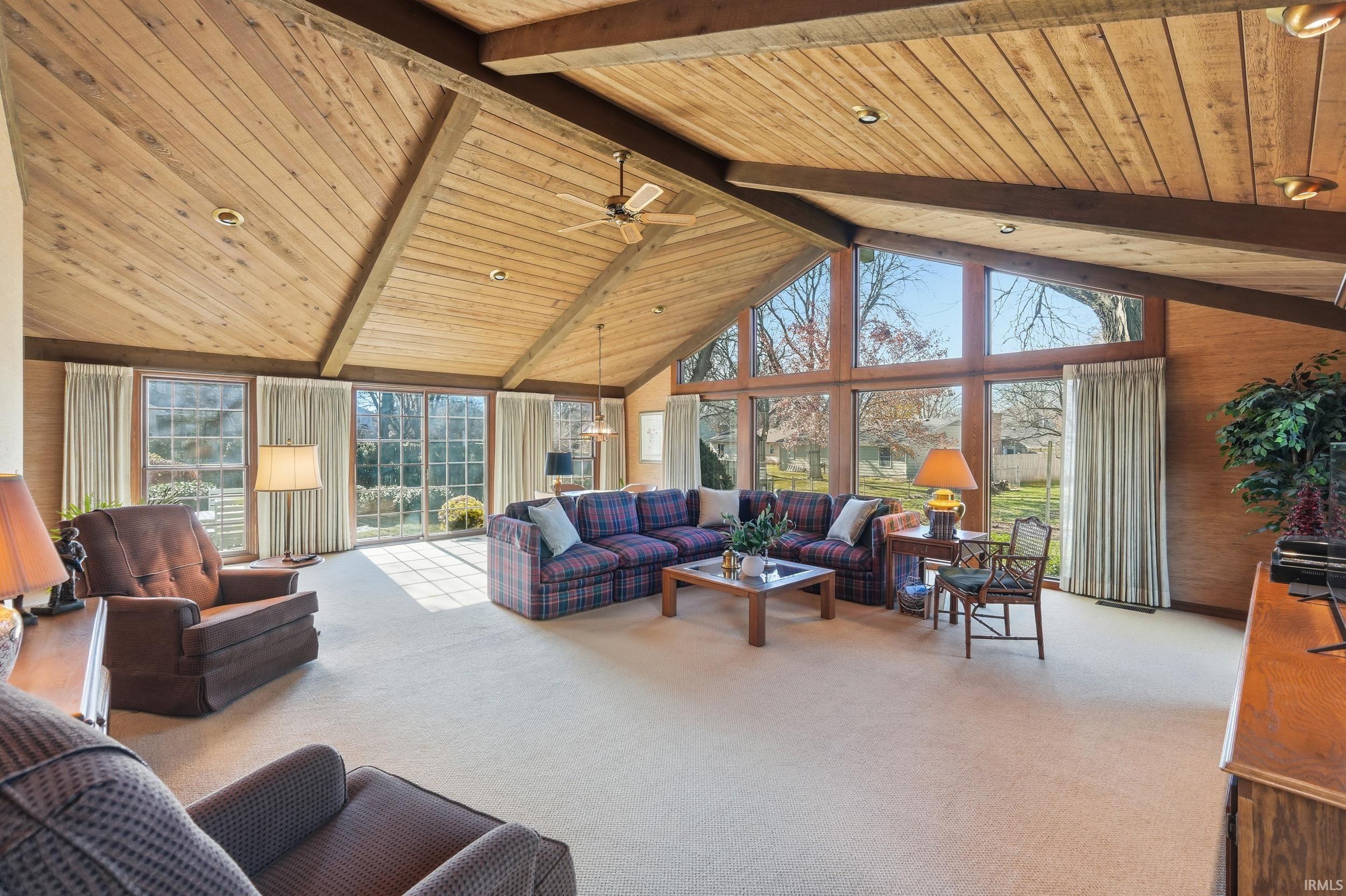 Living room featuring healthy amount of natural light, carpet, high vaulted ceiling, a wall of windows, and a wood ceiling with exposed beams