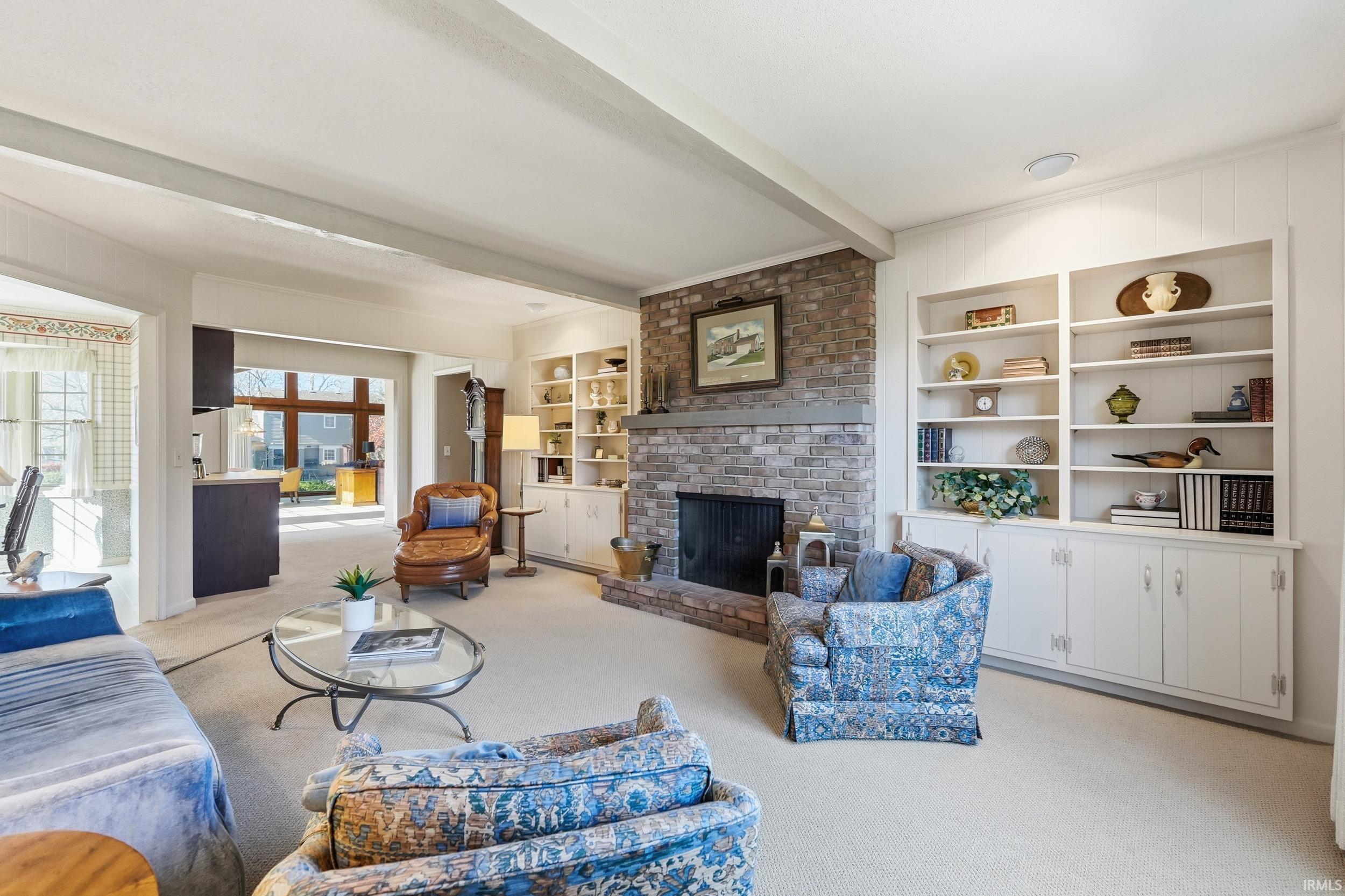 Living room with beamed ceiling, light colored carpet, a fireplace, and built in features