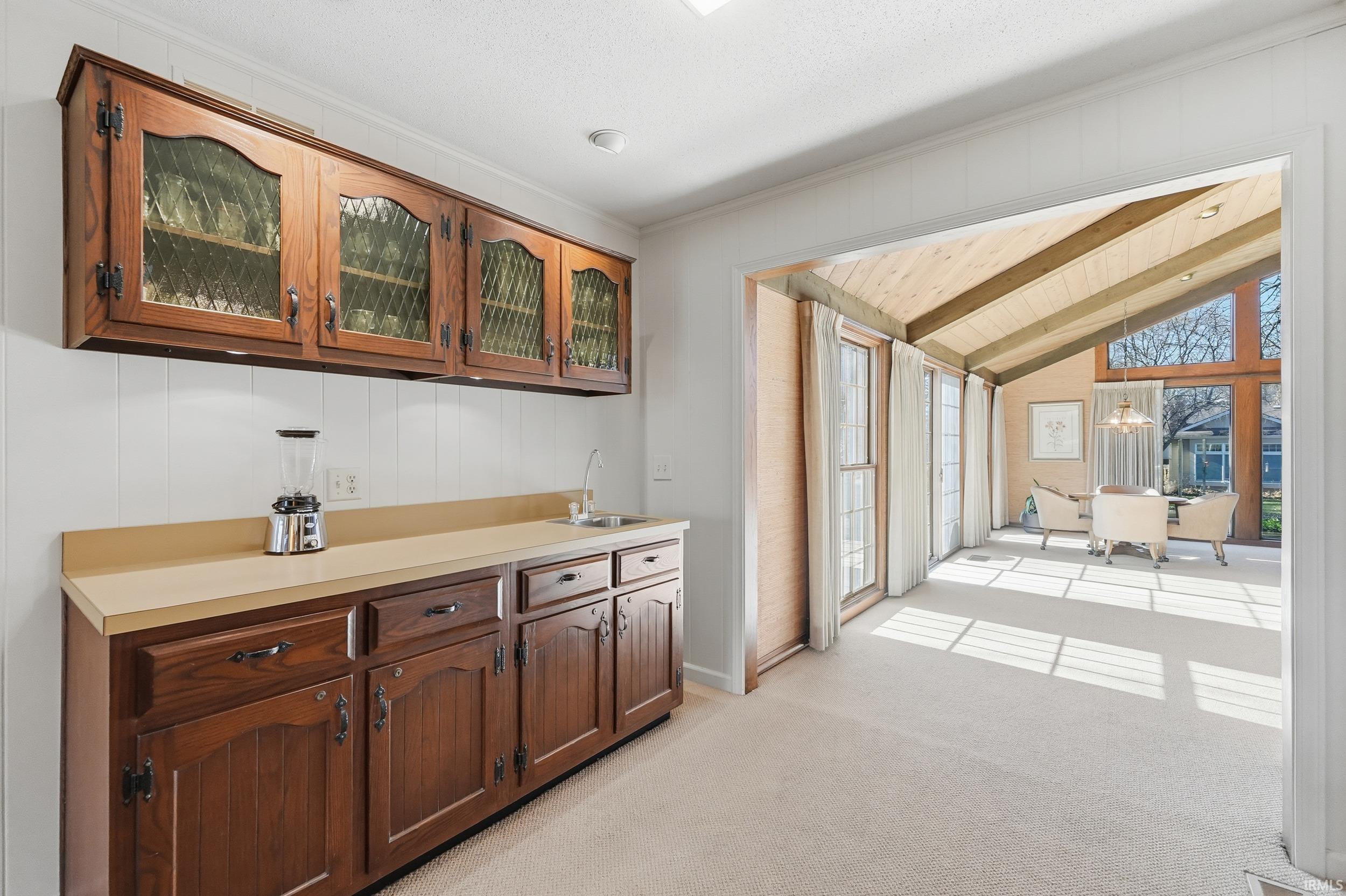 Bar featuring light countertops, glass insert cabinets, light colored carpet, wooden ceiling, and a sunroom