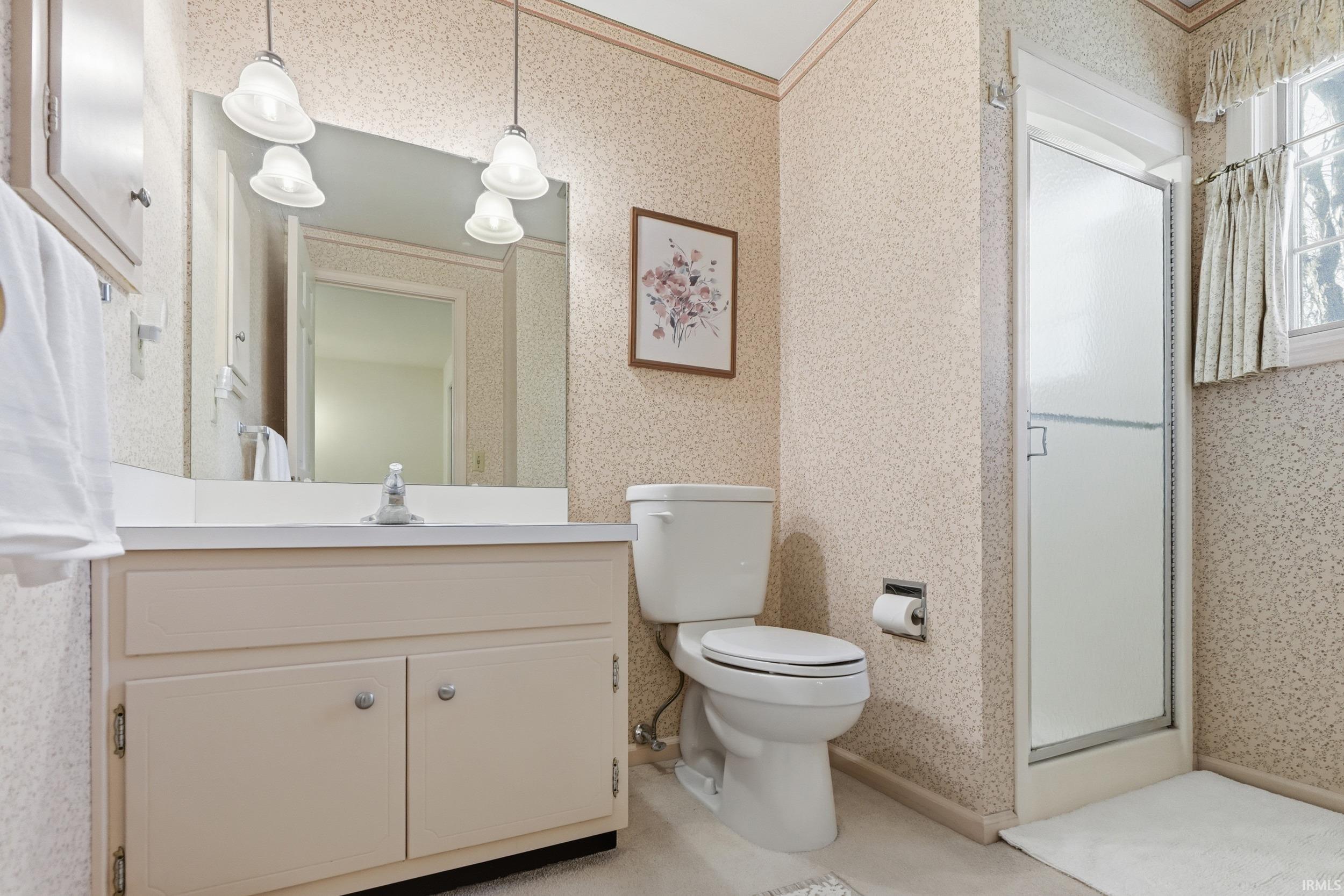 Bathroom with wallpapered walls, a shower stall, vanity, and crown molding