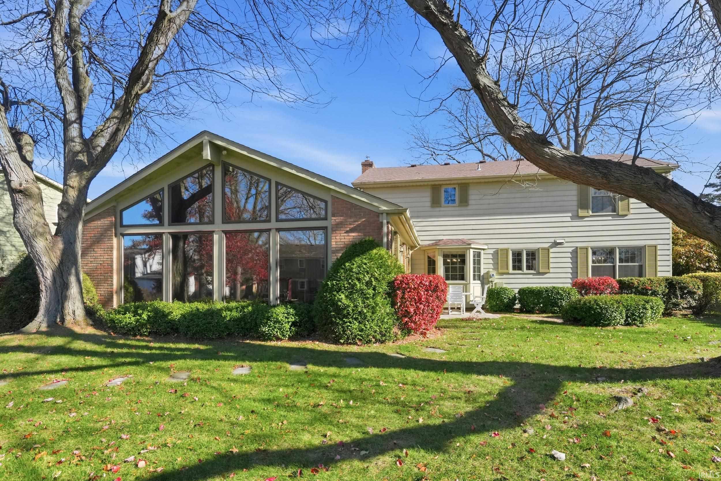 Back of property with a sunroom, a lawn, brick siding, and a chimney