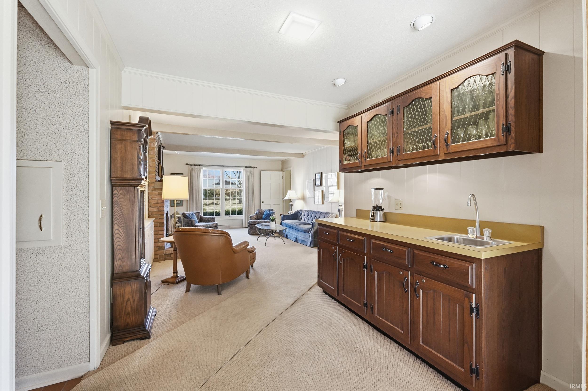 Bar featuring light countertops, ornamental molding, glass insert cabinets, dark brown cabinets, and light carpet