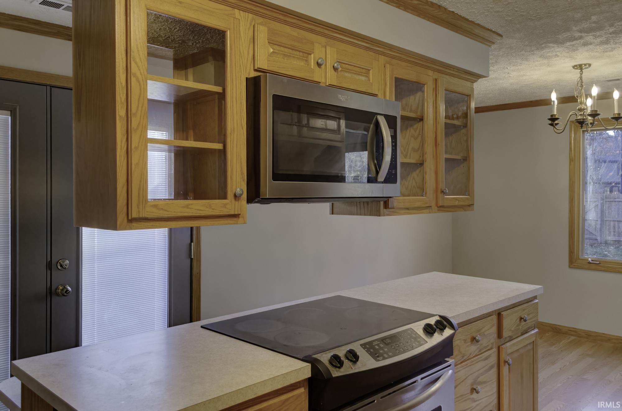 Kitchen with stainless steel appliances, ornamental molding, glass insert cabinets, light countertops, and a textured ceiling