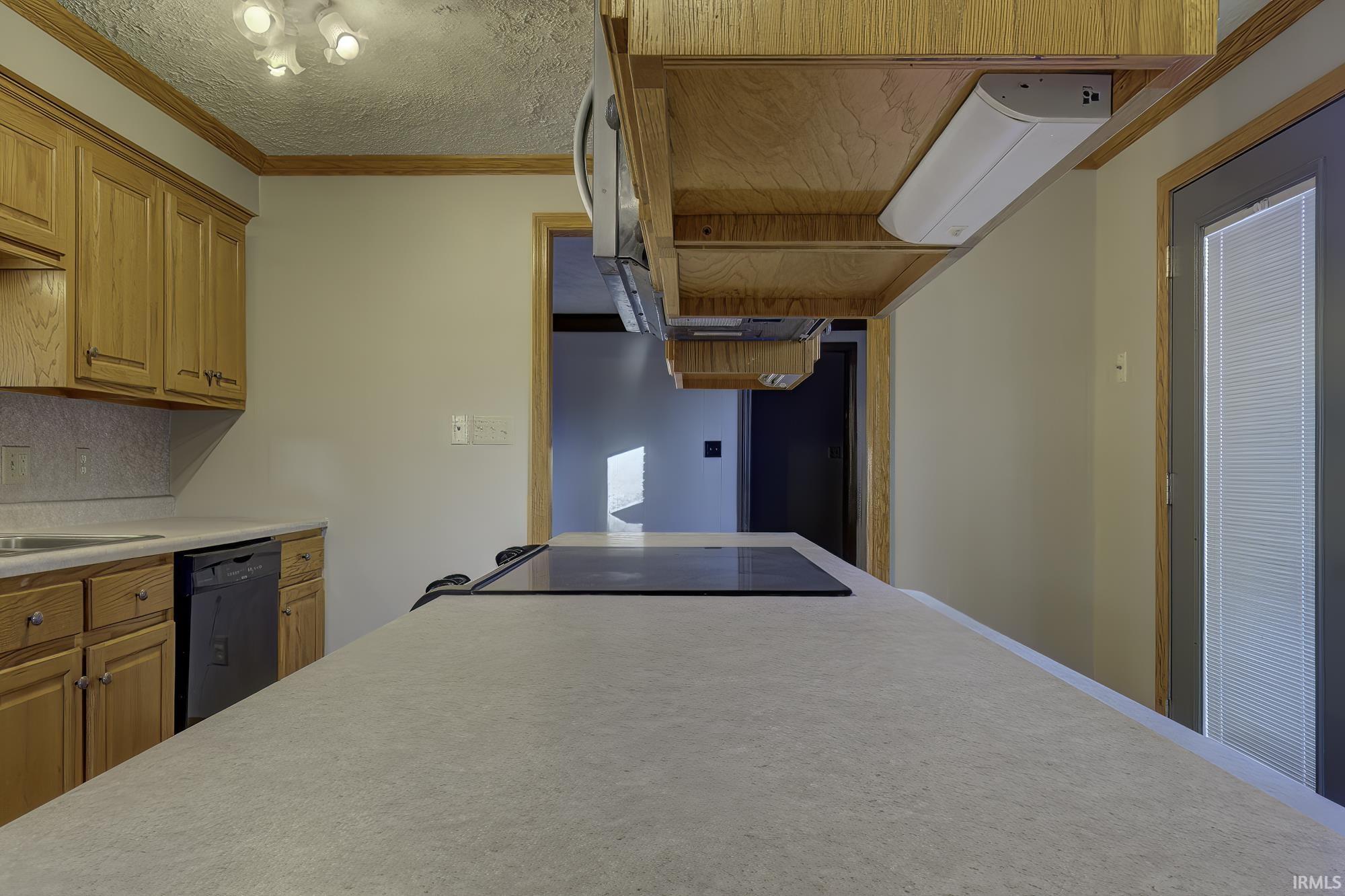 Kitchen with light countertops, ornamental molding, black dishwasher, a textured ceiling, and brown cabinetry