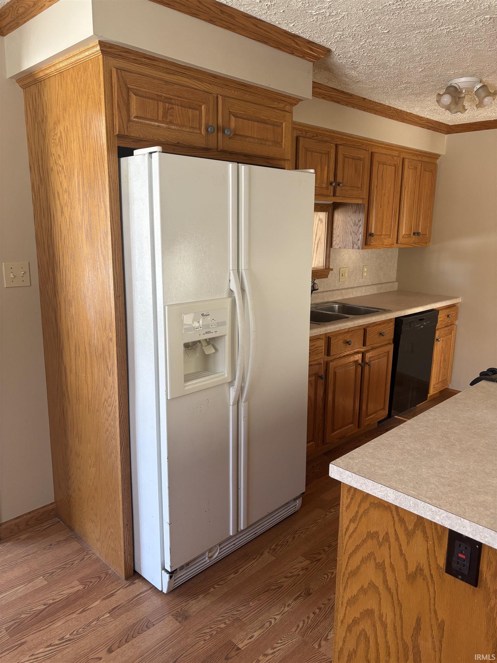 Kitchen with brown cabinets, light countertops, white fridge with ice dispenser, a textured ceiling, and dark wood finished floors
