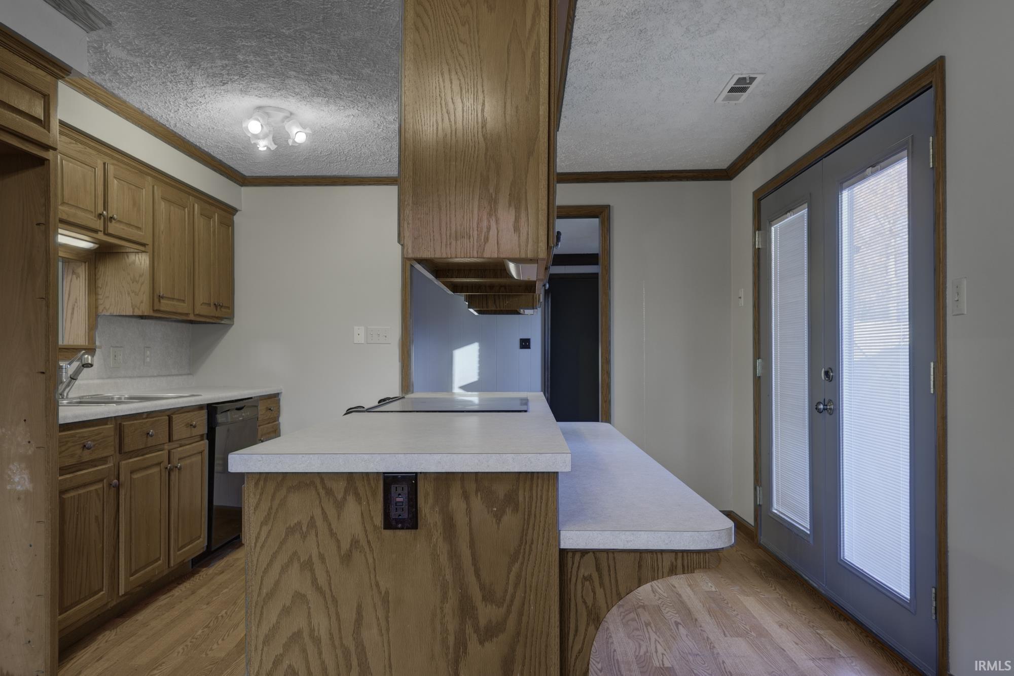 Kitchen with ornamental molding, brown cabinets, light wood-style floors, light countertops, and a textured ceiling