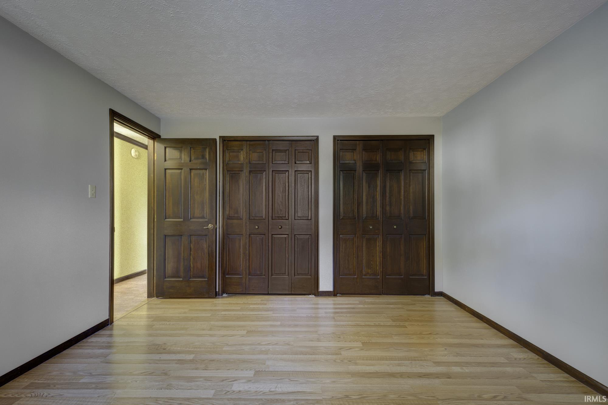 Unfurnished bedroom featuring light wood-style flooring, a textured ceiling, and multiple closets