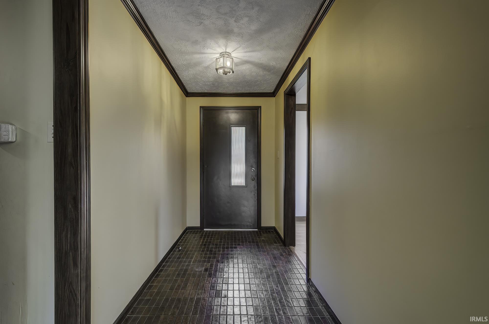 Doorway to outside with crown molding, a textured ceiling, and tile patterned flooring