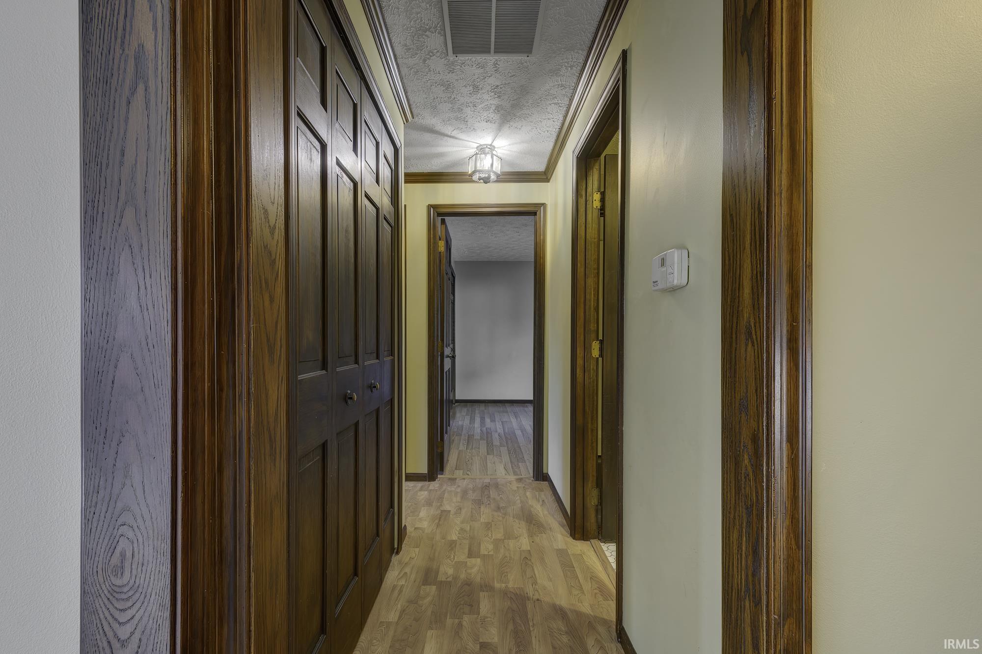Corridor featuring a textured ceiling, light wood finished floors, and crown molding