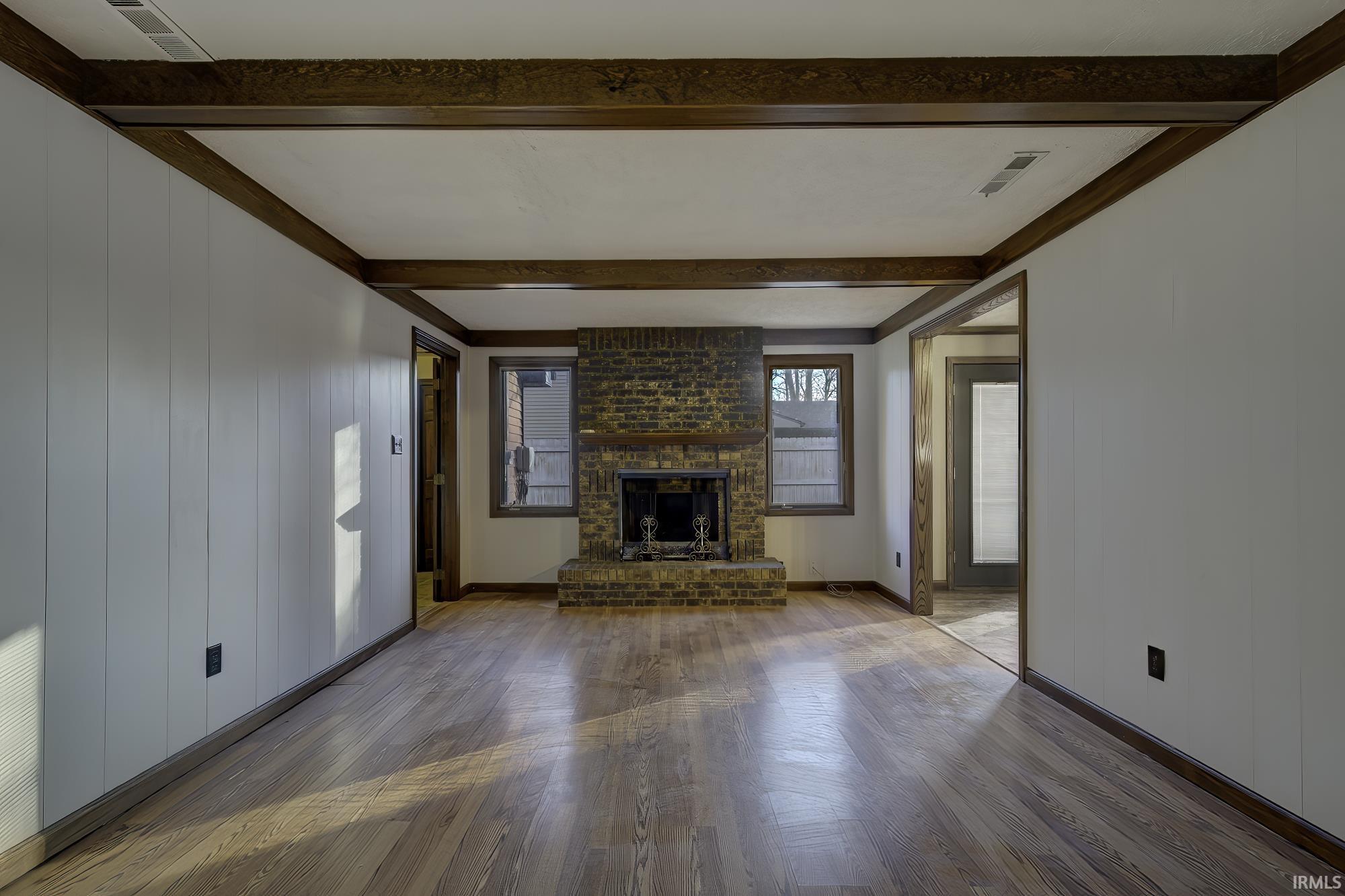 Unfurnished living room with wood finished floors, a fireplace, beam ceiling, and wooden walls