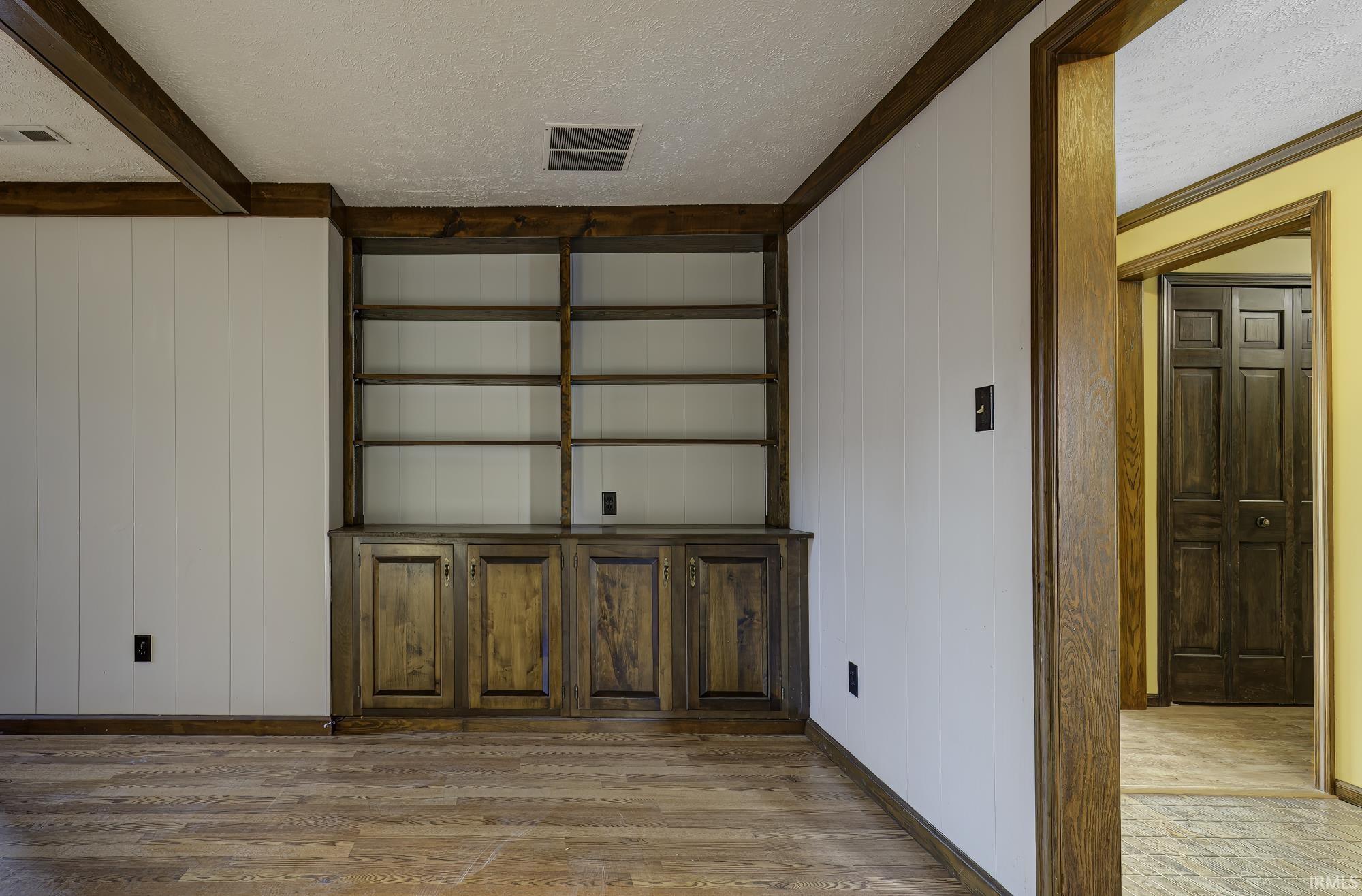 Unfurnished room with a textured ceiling, wooden walls, light wood-style flooring, and ornamental molding